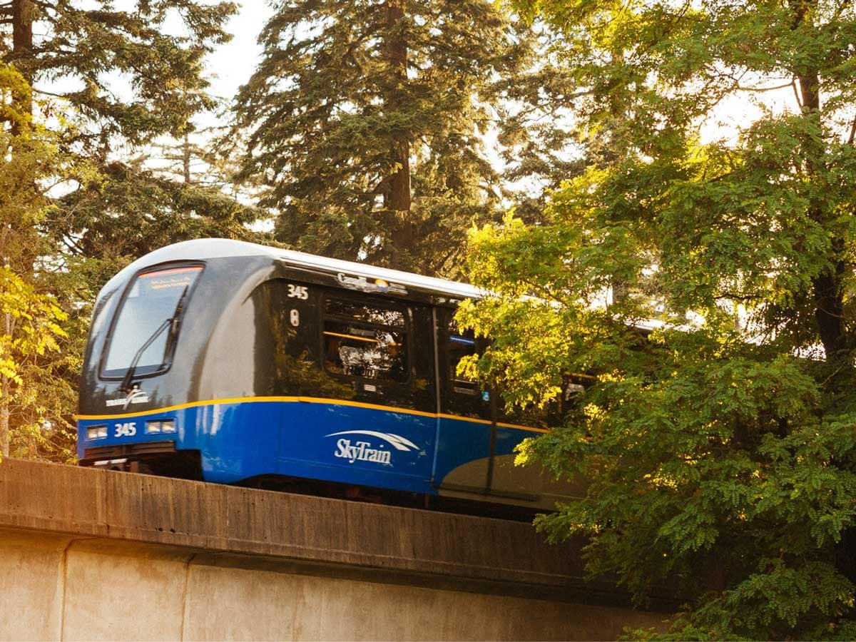 SkyTrain travelling through a tree-lined Burnaby neighbourhood, reflecting the transit accessibility connected to Burnaby presale condos and Burnaby new construction homes for sale.