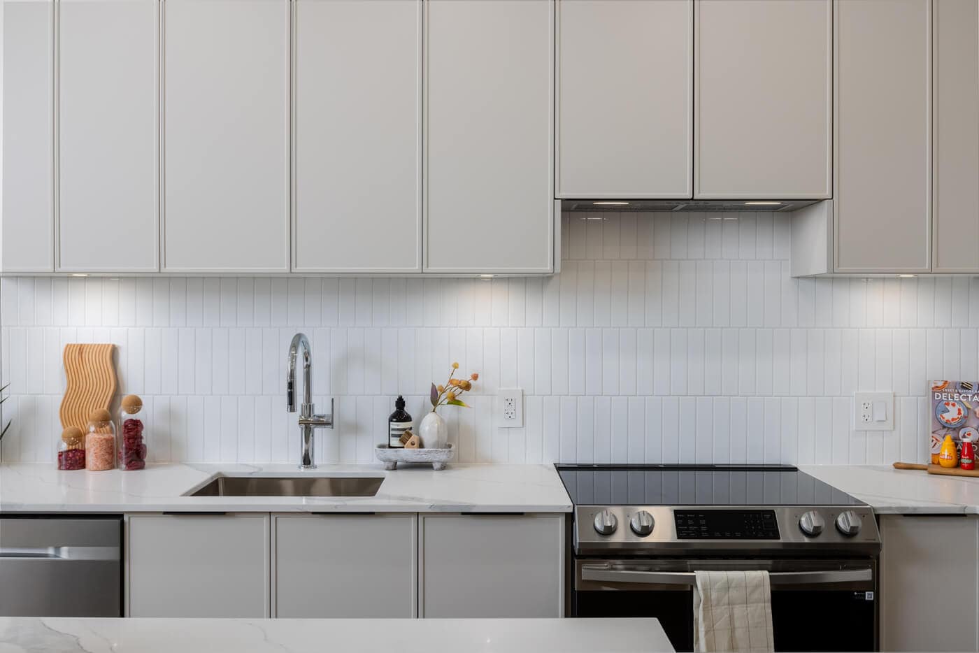 Contemporary kitchen finishes inside Jericho Park Langley condos by Essence Properties featuring quartz counters, tile backsplash, under-cabinet lighting, and stainless steel appliances at 19925 78B Avenue.