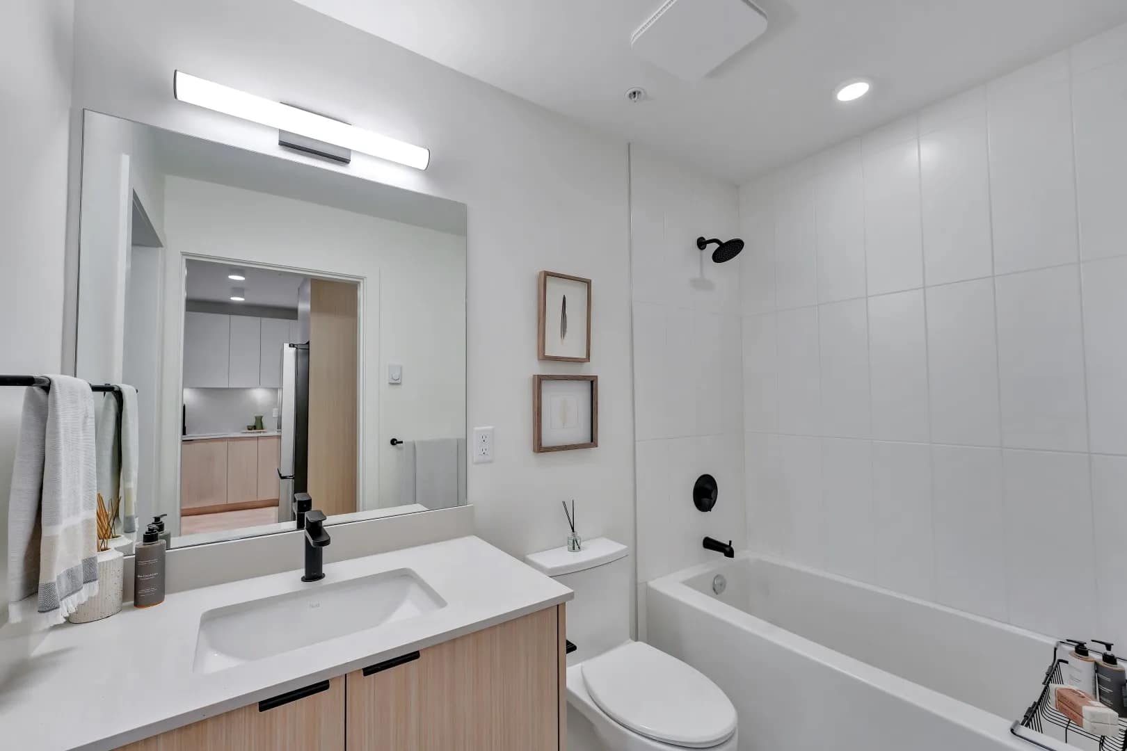 Bathroom at Jethro Langley in Langley City with modern vanity, large mirror, bathtub, black fixtures, and light wood cabinetry by Whitetail Homes.