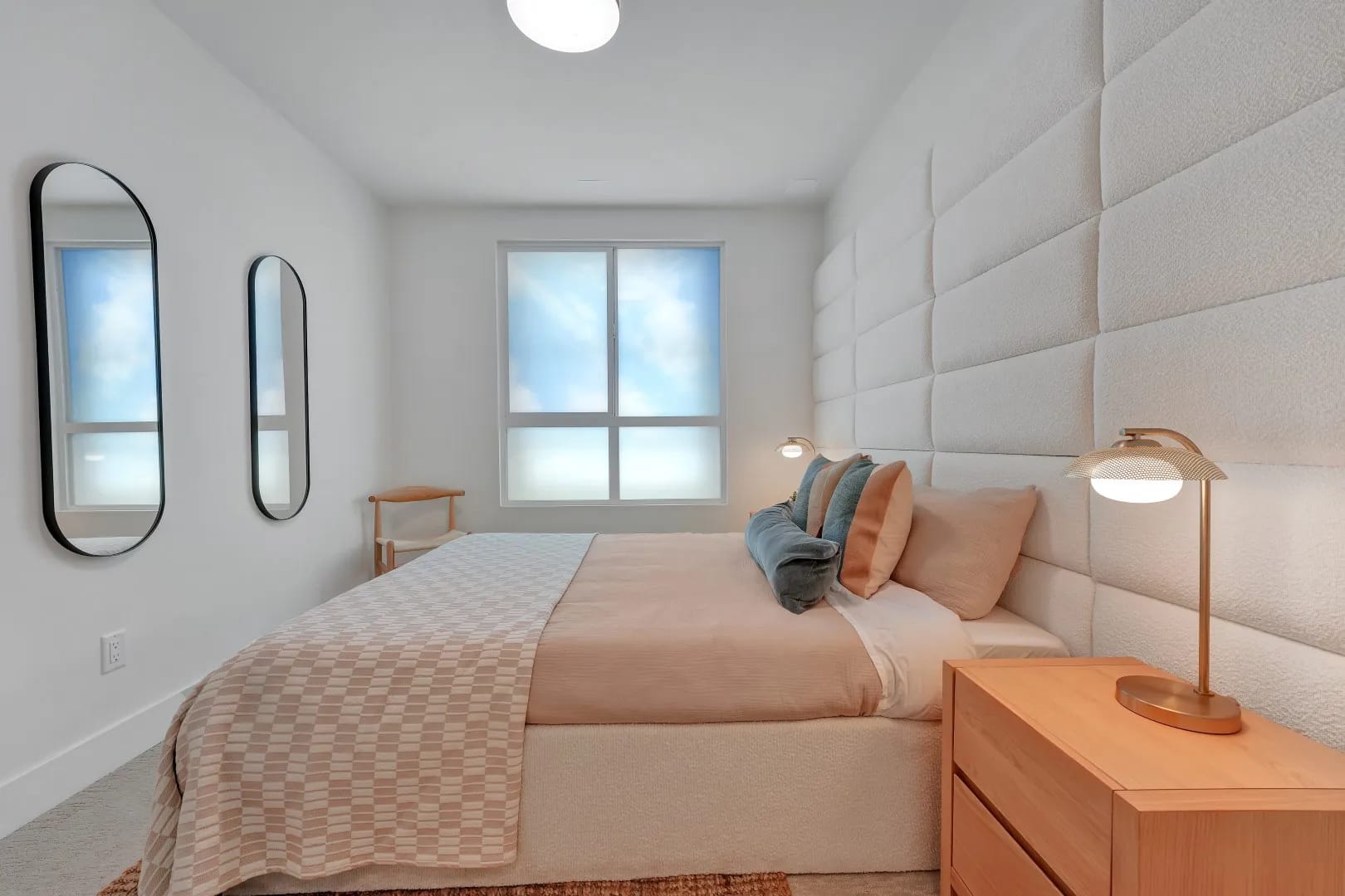 Bedroom at Jethro Langley in Langley City with upholstered feature wall, bedside lighting, soft neutral bedding, wall mirrors, and warm wood accents.