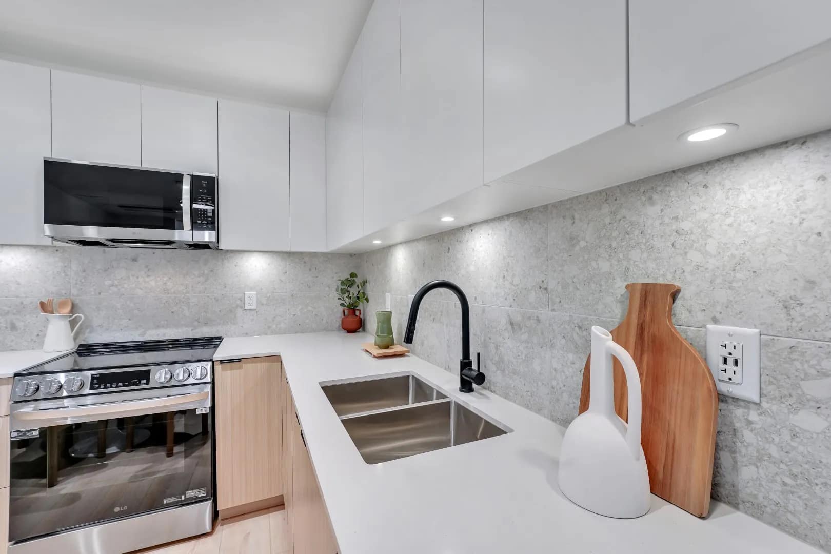 Kitchen detail at Jethro Langley showing quartz-style countertops, modern backsplash, undermount sink, black faucet, stainless steel appliances, and sleek cabinetry.