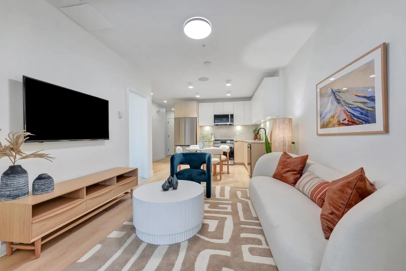 Open-concept living area at Jethro Langley Langley City with sofa, TV wall, accent chair, coffee table, and kitchen visible in the background.