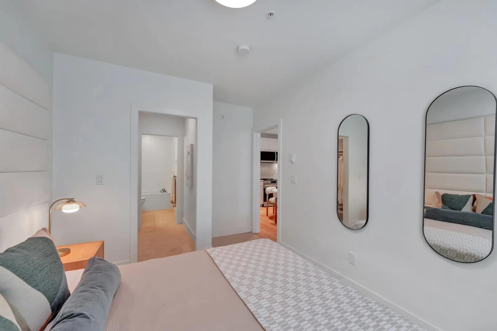 Primary bedroom at Jethro Langley Langley City showing a bed, wall mirrors, modern lighting, and views toward the bathroom and kitchen area.
