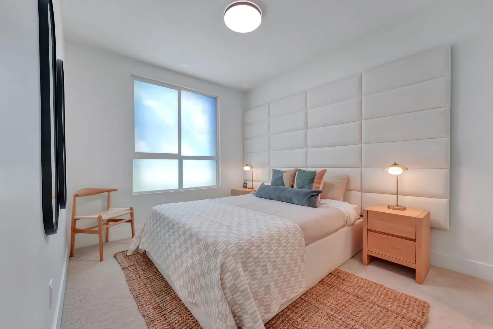Primary bedroom at Jethro Langley featuring a large window, upholstered feature wall, warm bedside tables, soft carpet, and neutral modern finishes.