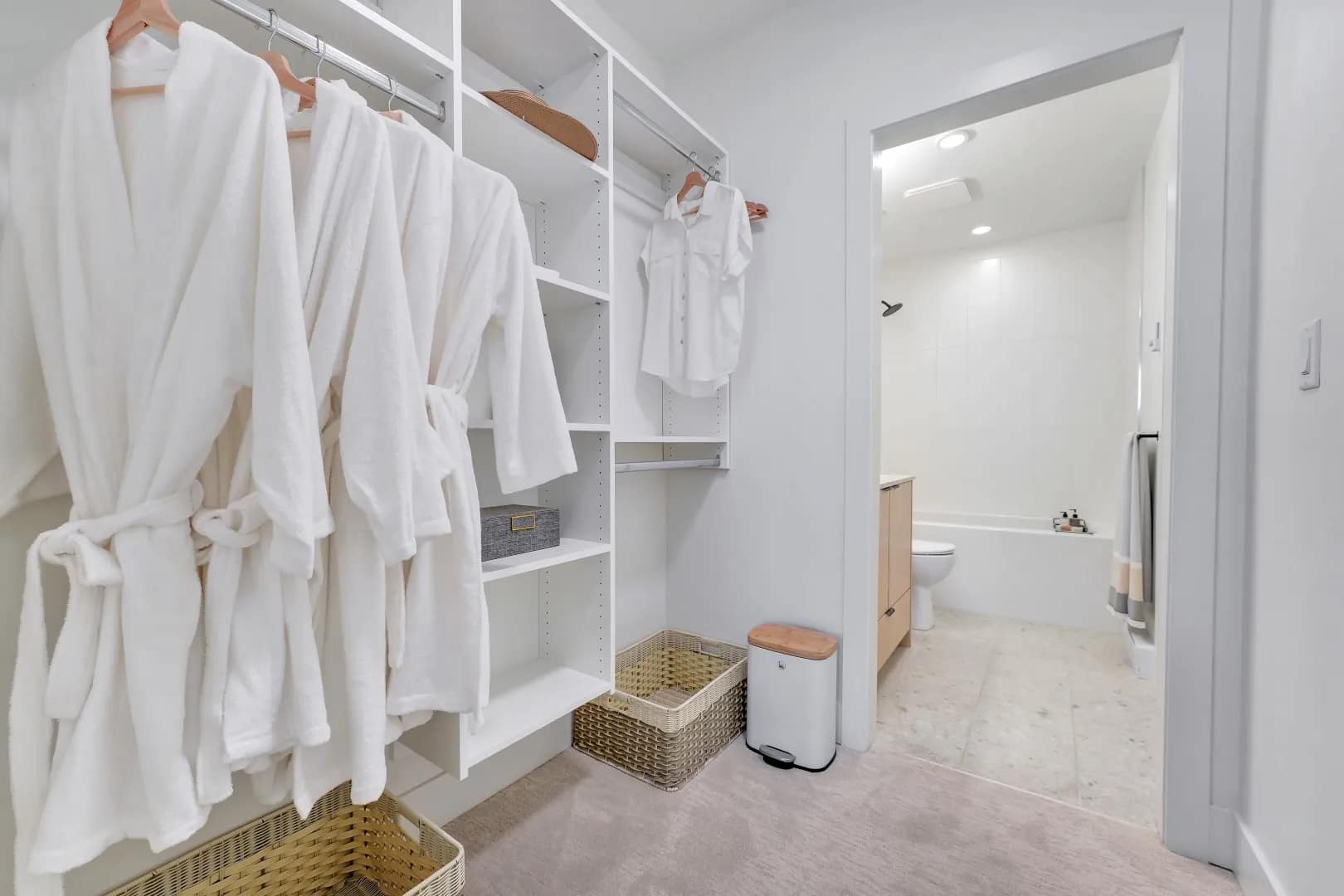 Walk-in closet at Jethro Langley showing open shelving, hanging space, storage baskets, and access to the bathroom in a Whitetail Homes condo.