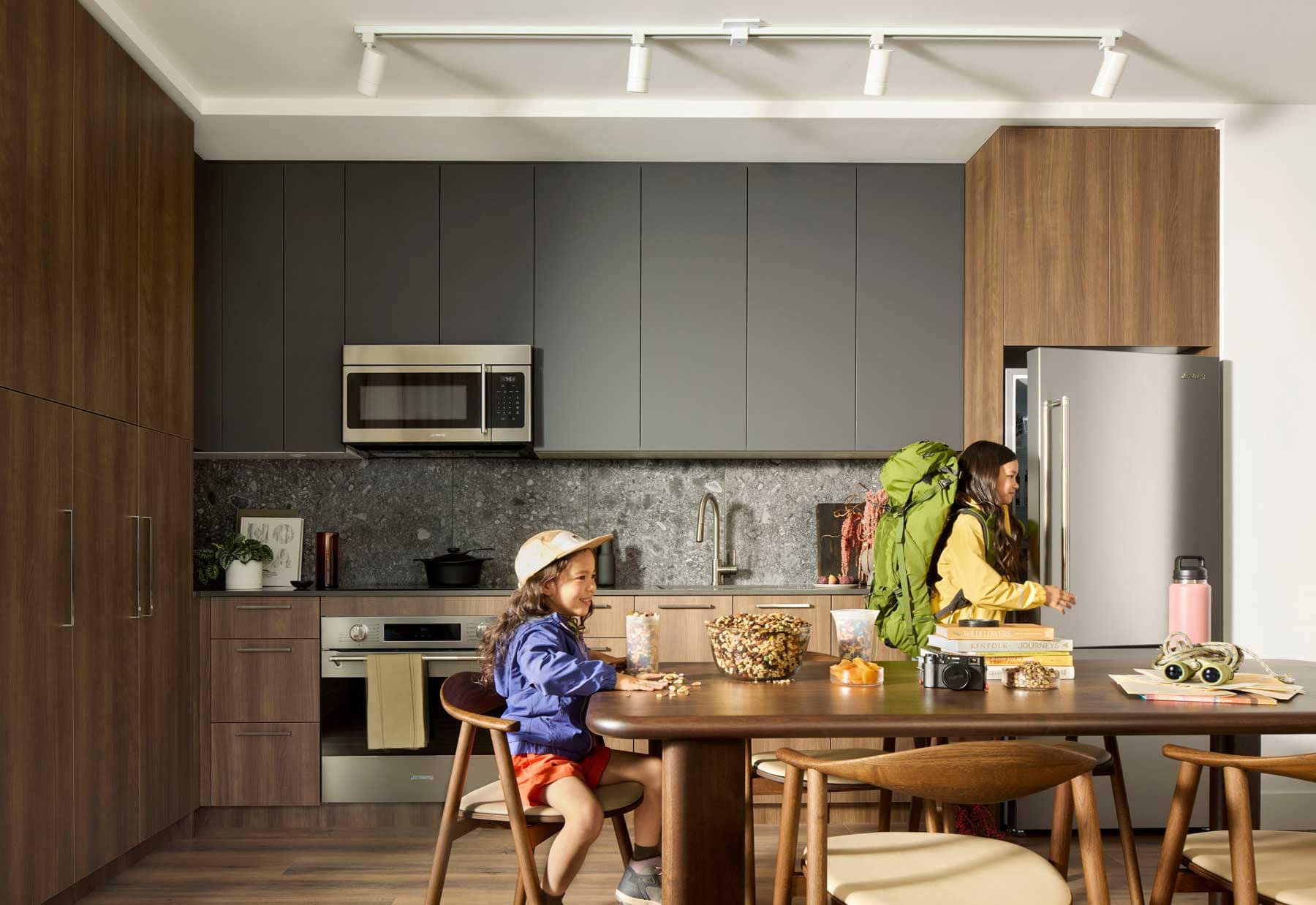 Family kitchen interior at Trailside at Lynn in North Vancouver featuring dark cabinetry, stone backsplash, large dining table, and modern appliances within a Mosaic-designed home at 2380 Emery Court.