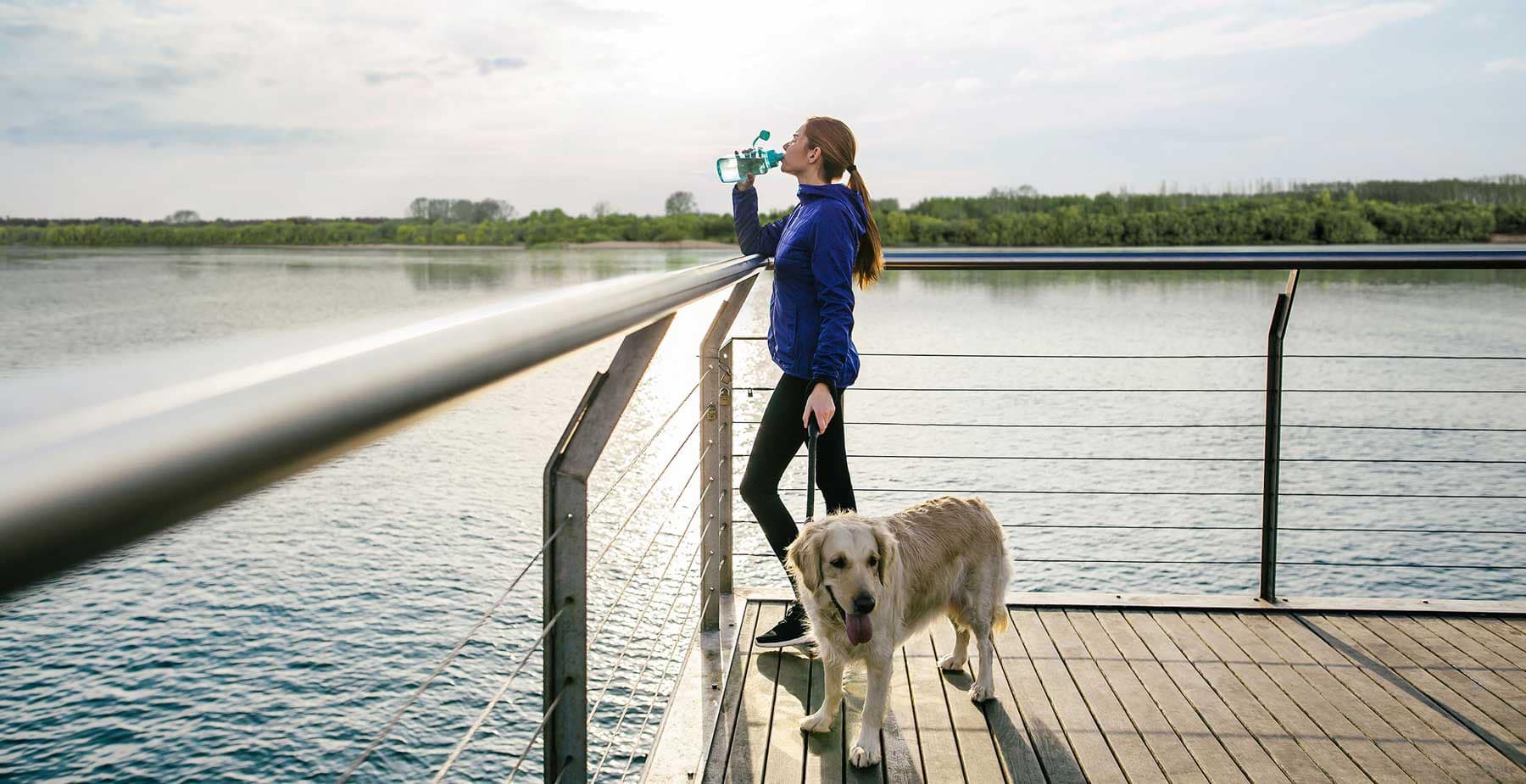 Resident enjoying the Fraser Mills waterfront boardwalk with a dog near Encore Coquitlam, highlighting riverfront recreation and outdoor lifestyle opportunities at 2 King Edward Street.