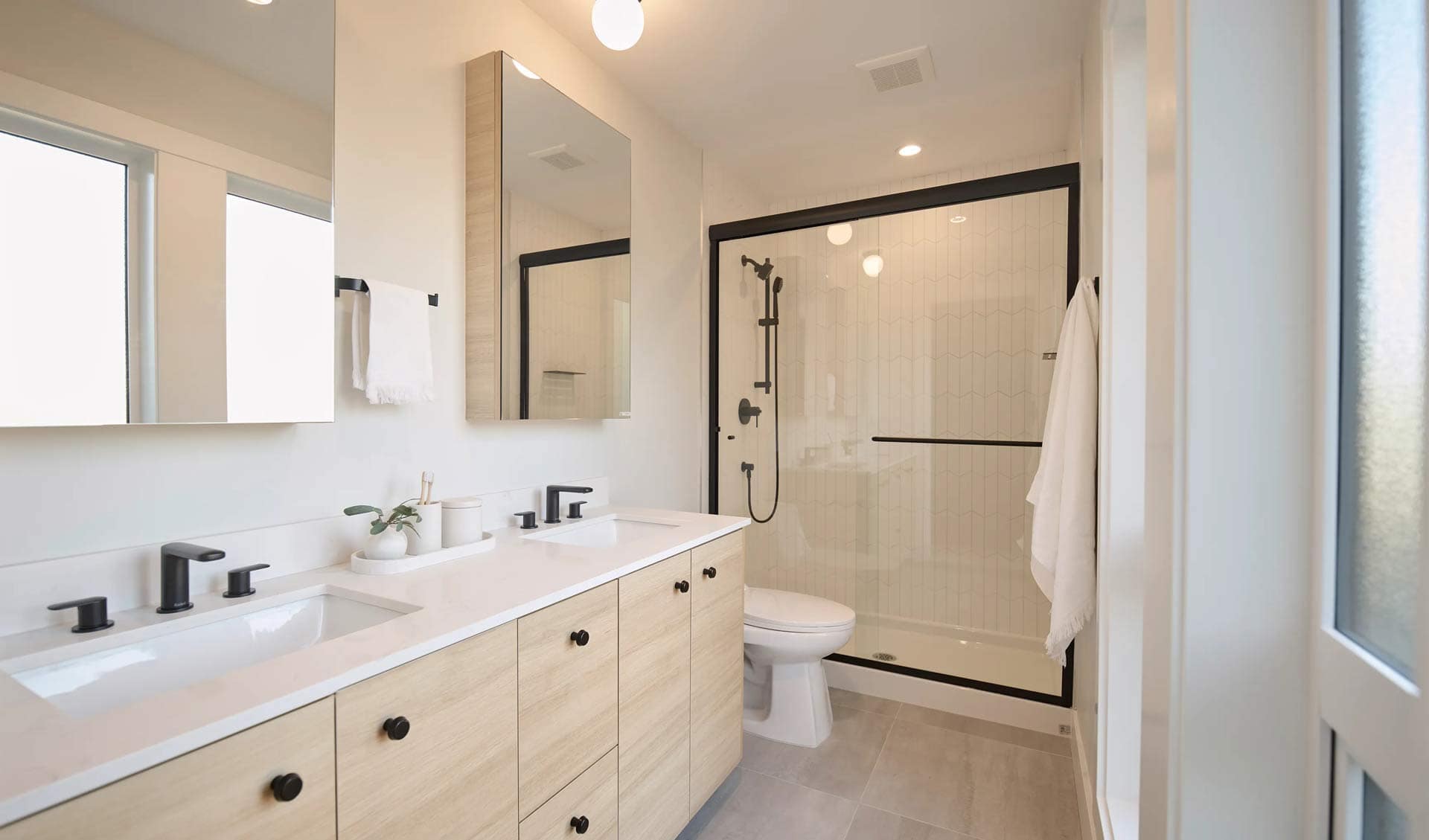 Primary bathroom at Addition Langley in Willoughby Langley by Redekop Ferrario Properties featuring double vanity, black fixtures, glass shower enclosure, and modern tile finishes