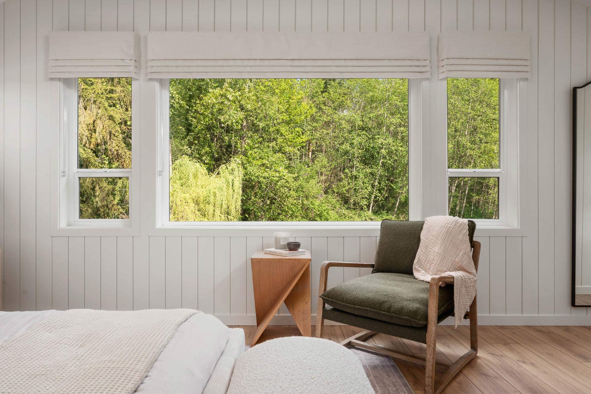 Bedroom at Haven Maple Ridge by Epic Homes at 11205 250B Street with large windows overlooking trees, accent chair, and wood flooring