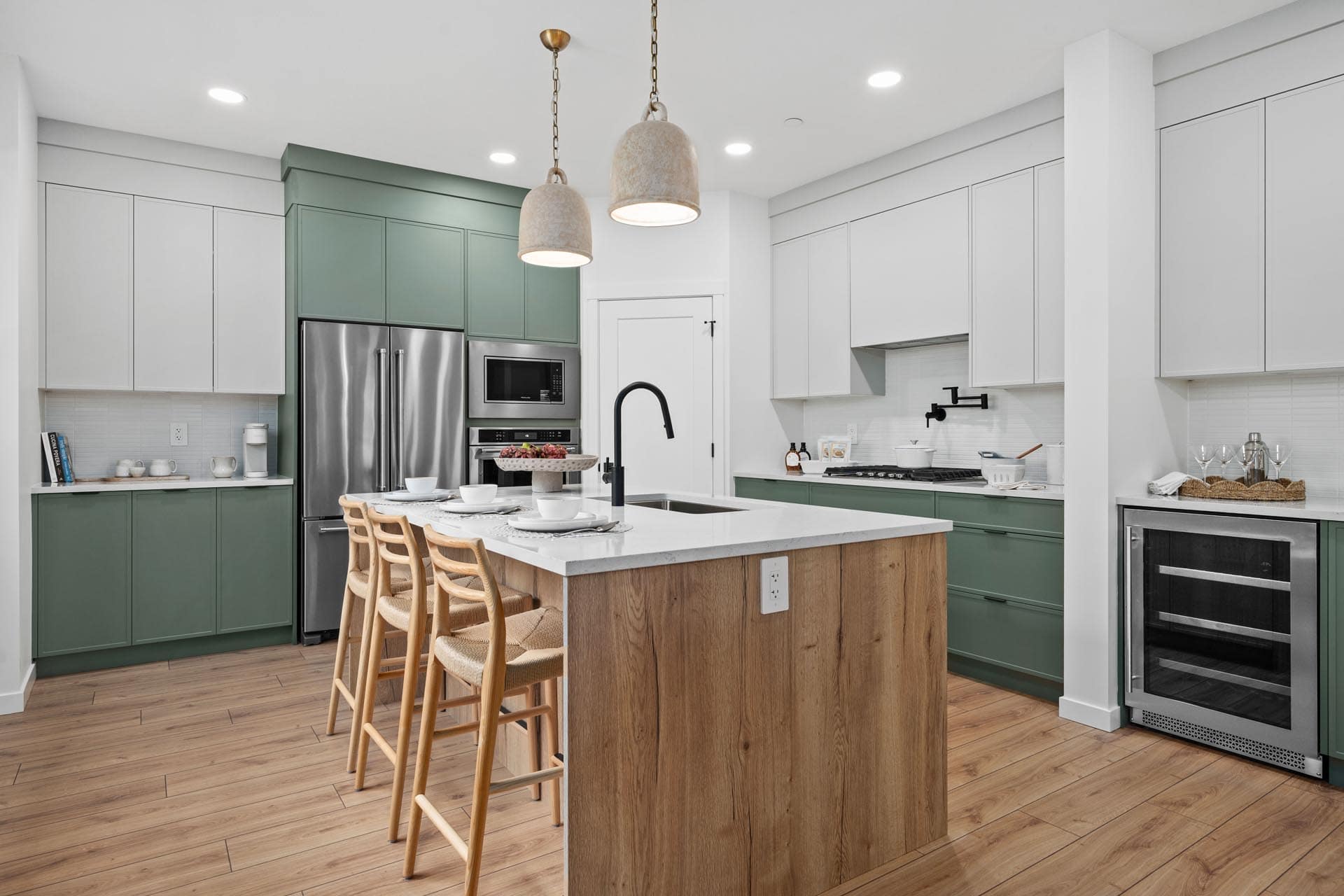 Modern kitchen at Haven Maple Ridge by Epic Homes at 11205 250B Street featuring green cabinetry, white quartz island, pendant lighting, and stainless steel appliances