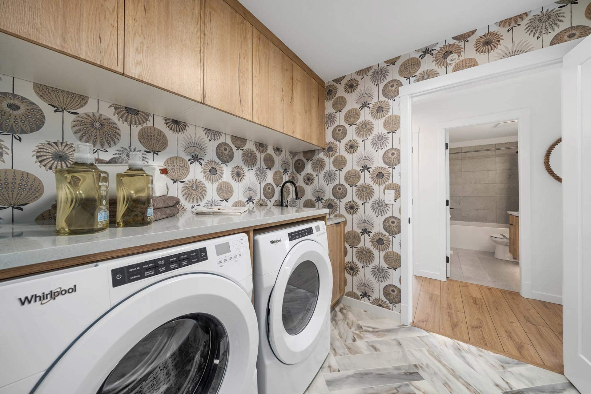 Laundry room at Haven Maple Ridge by Epic Homes at 11205 250B Street featuring washer, dryer, wood cabinetry, and patterned wallpaper
