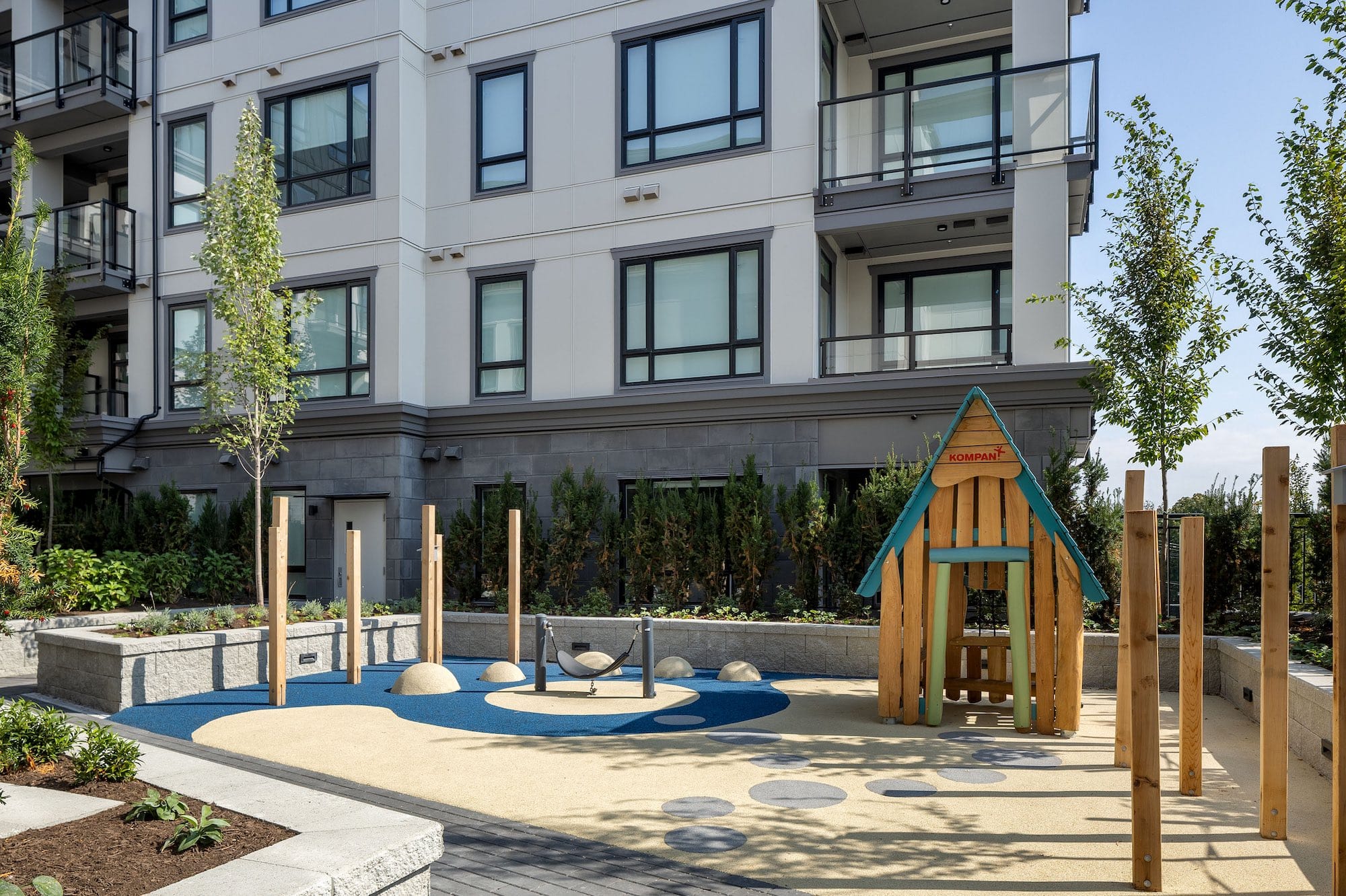 Children’s playground courtyard at Bastille presale condominiums by Porte Homes in Coquitlam’s Maillardville neighbourhood featuring a modern play structure, climbing elements, soft safety surfacing, landscaped planters, and the residential building exterior in the background at 209 Lebleu Street.