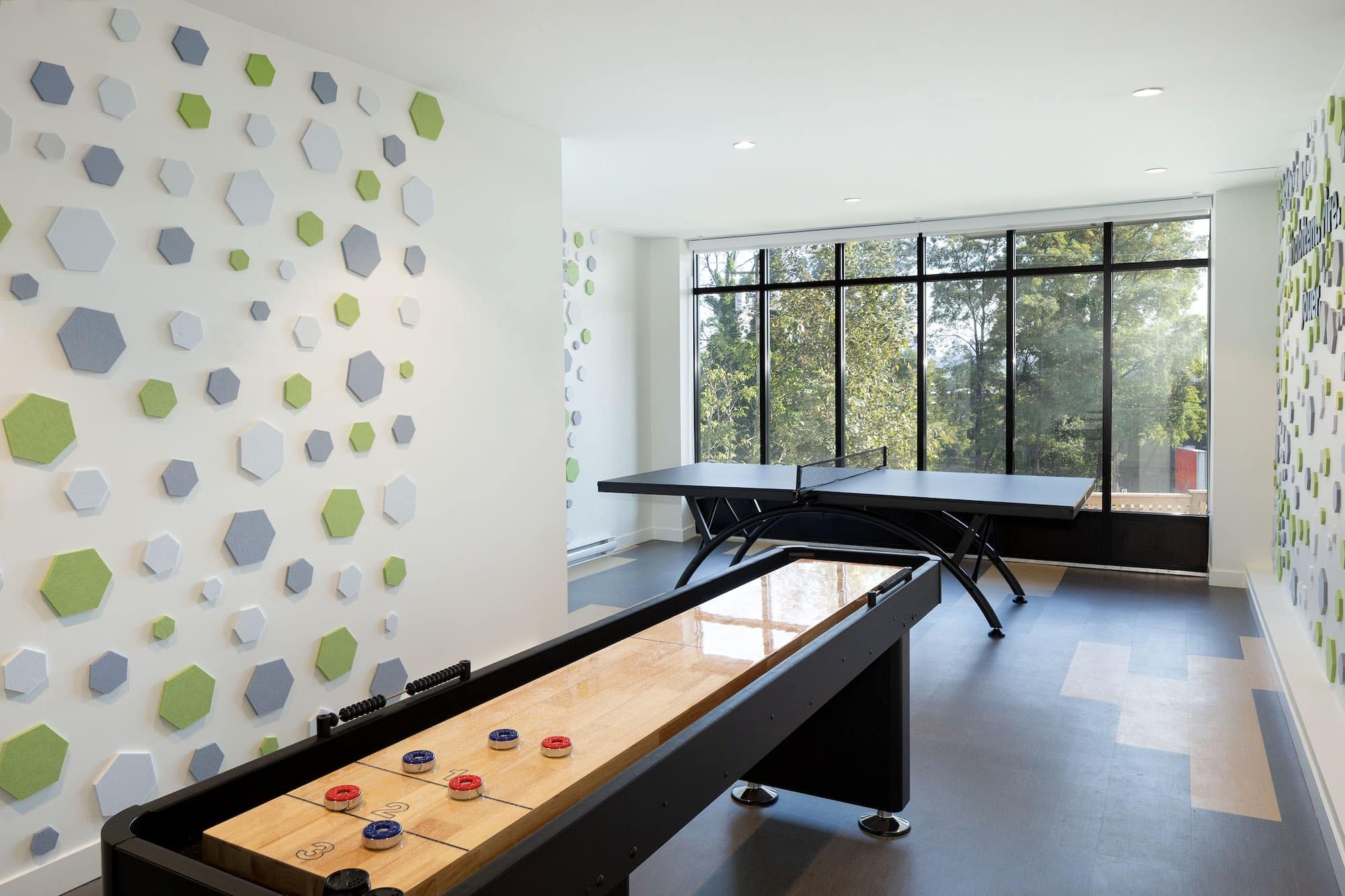 Resident games and recreation room at Bastille presale condos by Porte Homes in Coquitlam’s Maillardville neighbourhood featuring a shuffleboard table, ping pong table, and large windows providing natural light in the community amenity space at 209 Lebleu Street.