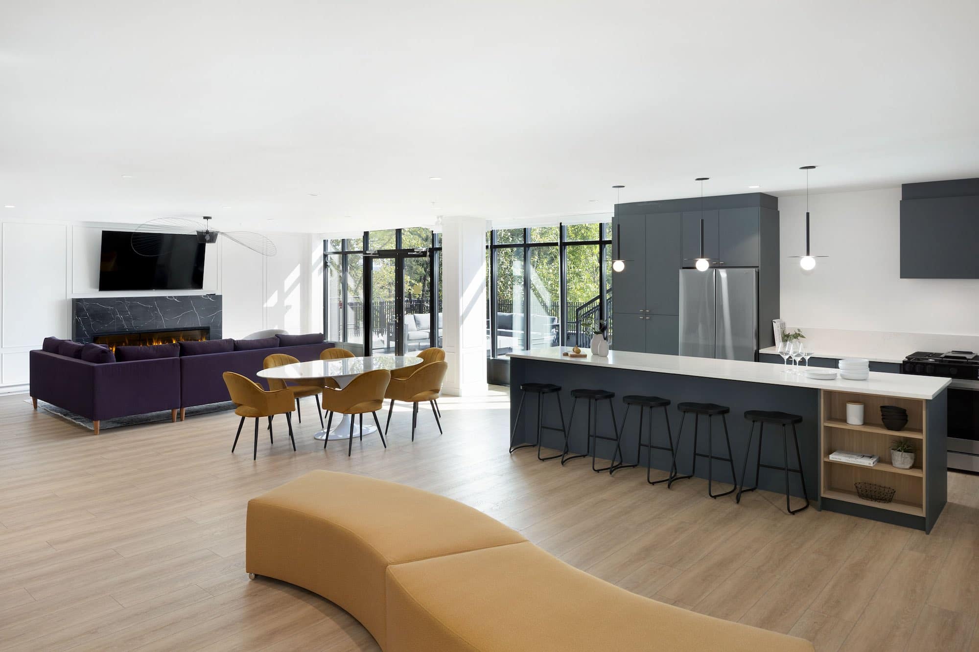Large resident lounge and entertainment space at Bastille presale development by Porte Homes in Coquitlam’s Maillardville neighbourhood featuring a full kitchen, dining area, lounge seating, fireplace, and large windows overlooking landscaped outdoor spaces at 209 Lebleu Street.