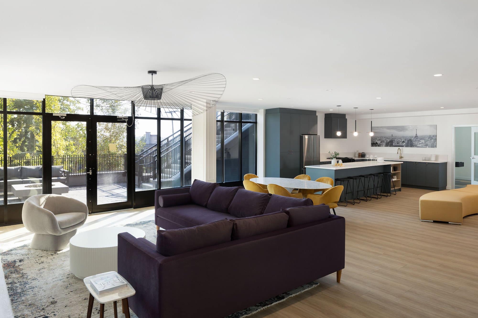 Resident lounge and entertainment space at Bastille presale development by Porte Homes located at 209 Lebleu Street in Coquitlam’s Maillardville neighbourhood featuring an open-concept living area with modern sofas, designer lighting, large windows, a communal dining table, and a full kitchen with island seating designed for social gatherings and resident events.