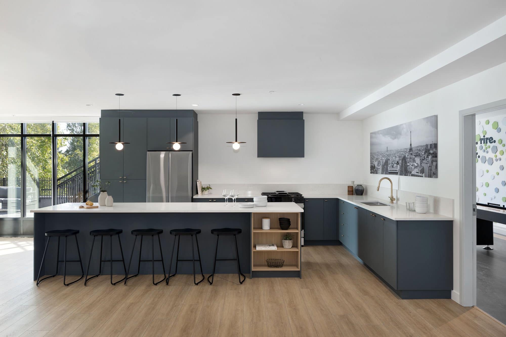 Modern shared kitchen and lounge amenity at Bastille presale condominiums by Porte Homes in Coquitlam’s Maillardville neighbourhood featuring a large island with bar seating, contemporary cabinetry, stainless appliances, pendant lighting, and spacious open floor layout within the resident amenity area at 209 Lebleu Street.