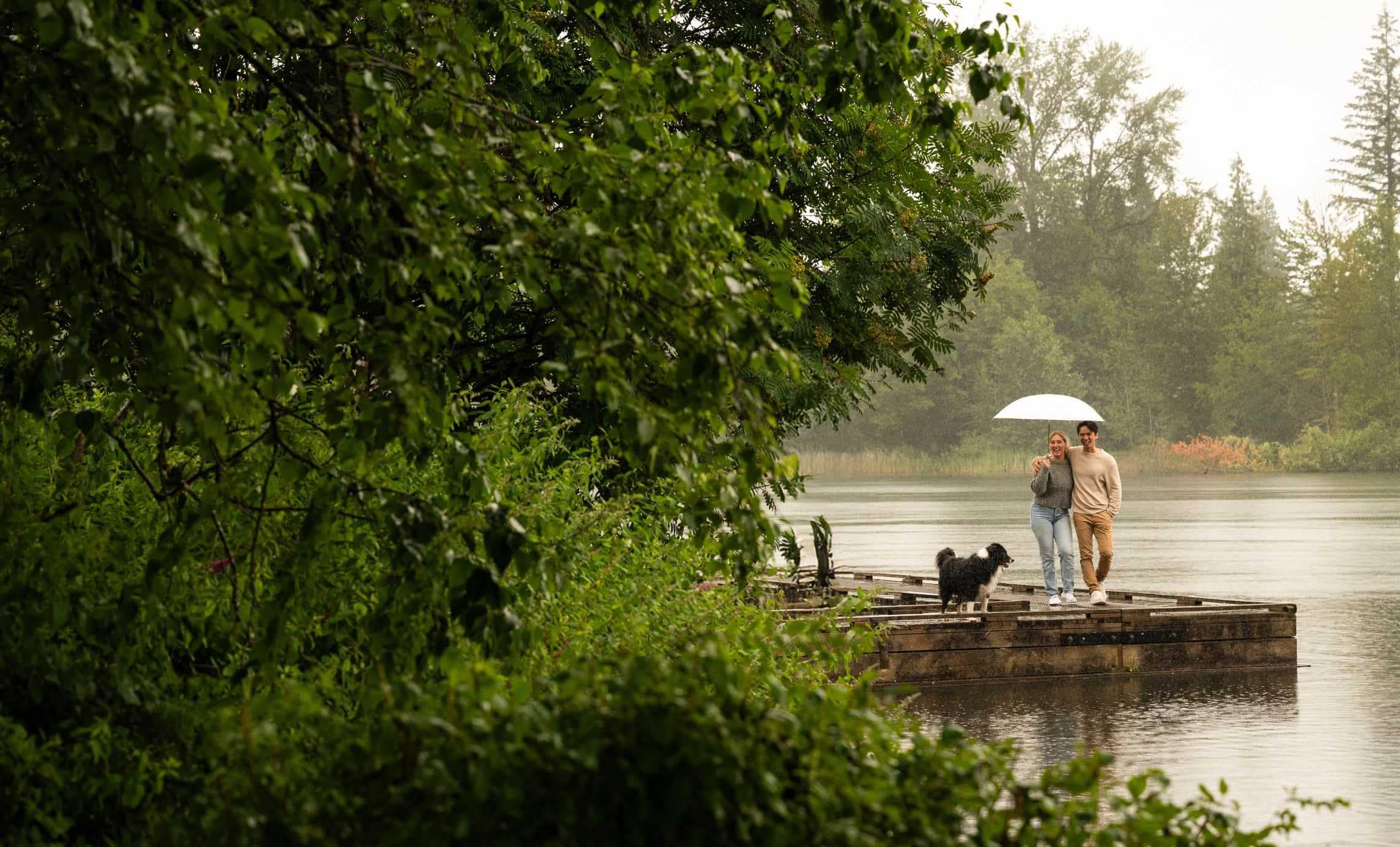 Lifestyle image near Goldfinch presale development in Coquitlam West showing a couple walking with a dog along a lakeside boardwalk, highlighting access to nature, trails, and outdoor recreation near 628 Smith Avenue.