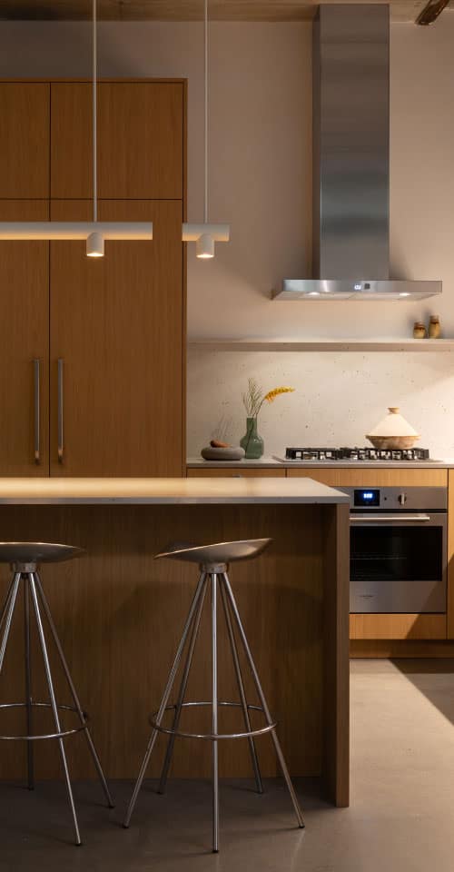 Modern kitchen at Hem Vancouver by Hudson featuring warm wood cabinetry, island with bar seating, stainless steel appliances, and minimalist lighting at 385 Lakewood Drive Vancouver East