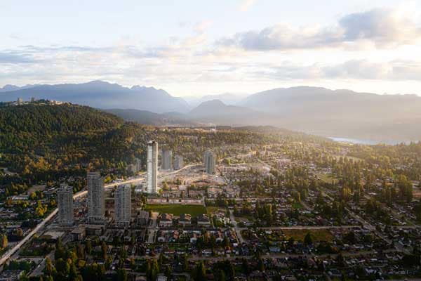 Aerial view of Burquitlam and Coquitlam surrounding Jinju by Anthem Properties at 533 Cottonwood Avenue, showing residential neighbourhoods, high-rise buildings, SkyTrain corridor, and mountain backdrop at sunset.