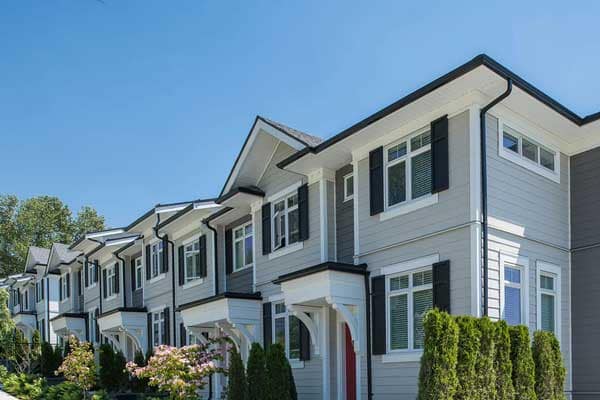 Street view of contemporary townhomes at Chelsea at The Boroughs presale development in Surrey’s Sunnyside Heights neighbourhood, developed by Northwest Development at 16325 21 Avenue, featuring modern West Coast architecture with grey siding, white trim, black shutters, pitched roofs, and landscaped walkways along a pedestrian-friendly community street.