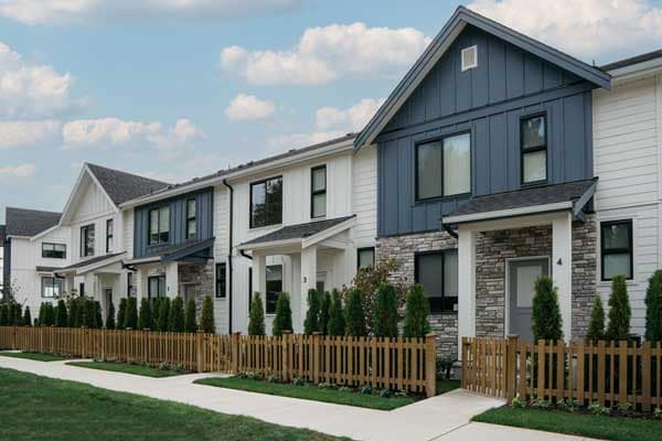 Exterior streetscape of Fox & Aikins townhomes in South Surrey by Park Ridge Homes, located at 1871 165A Street, featuring modern farmhouse architecture with board and batten siding, stone accents, pitched rooflines, landscaped front yards, and wood picket fencing along a pedestrian-friendly sidewalk.