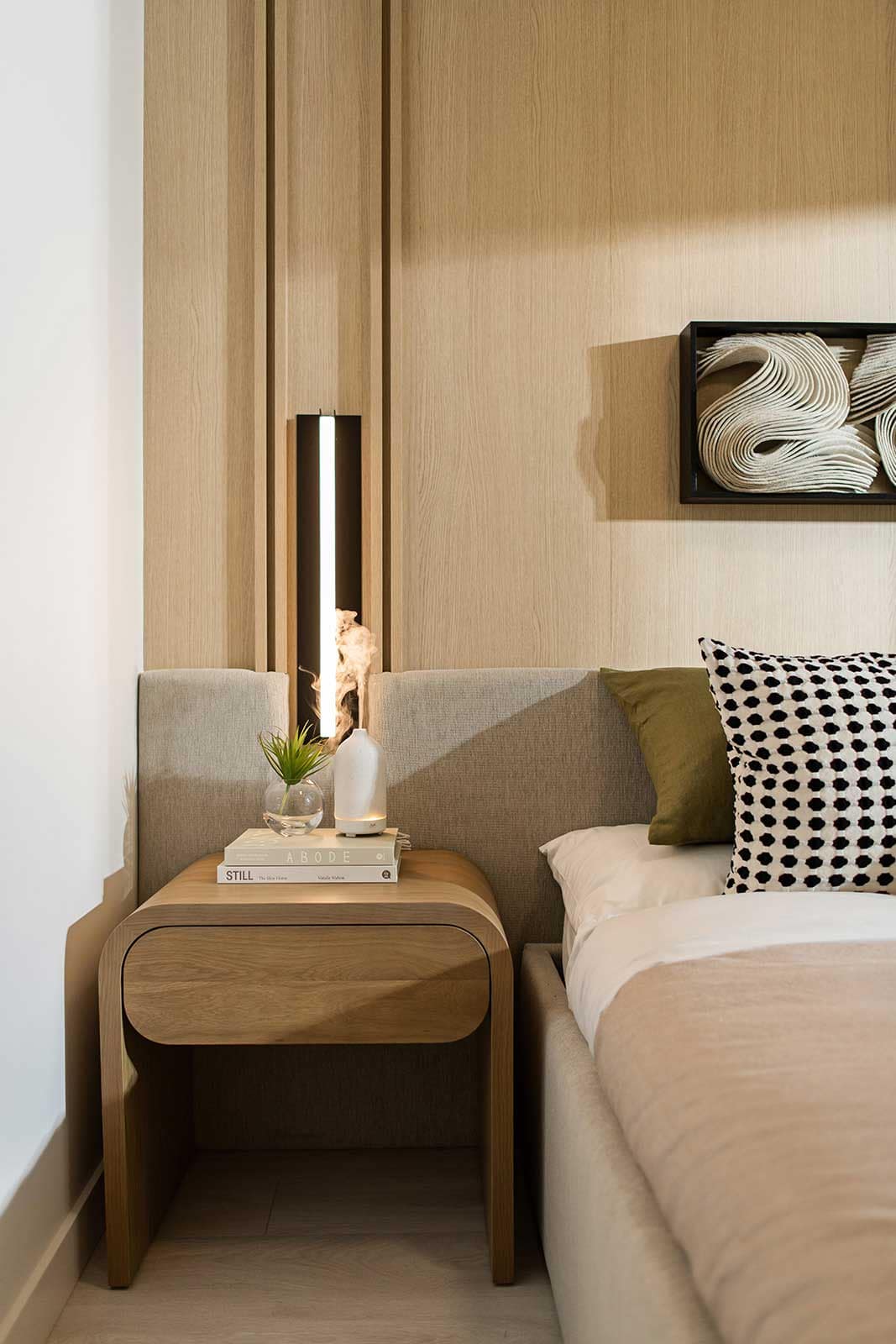 Close-up bedroom detail at Jinju Coquitlam condos by Anthem Properties in Burquitlam, featuring wood nightstand, modern lighting, textured wall panels, and curated decor reflecting contemporary interior design.
