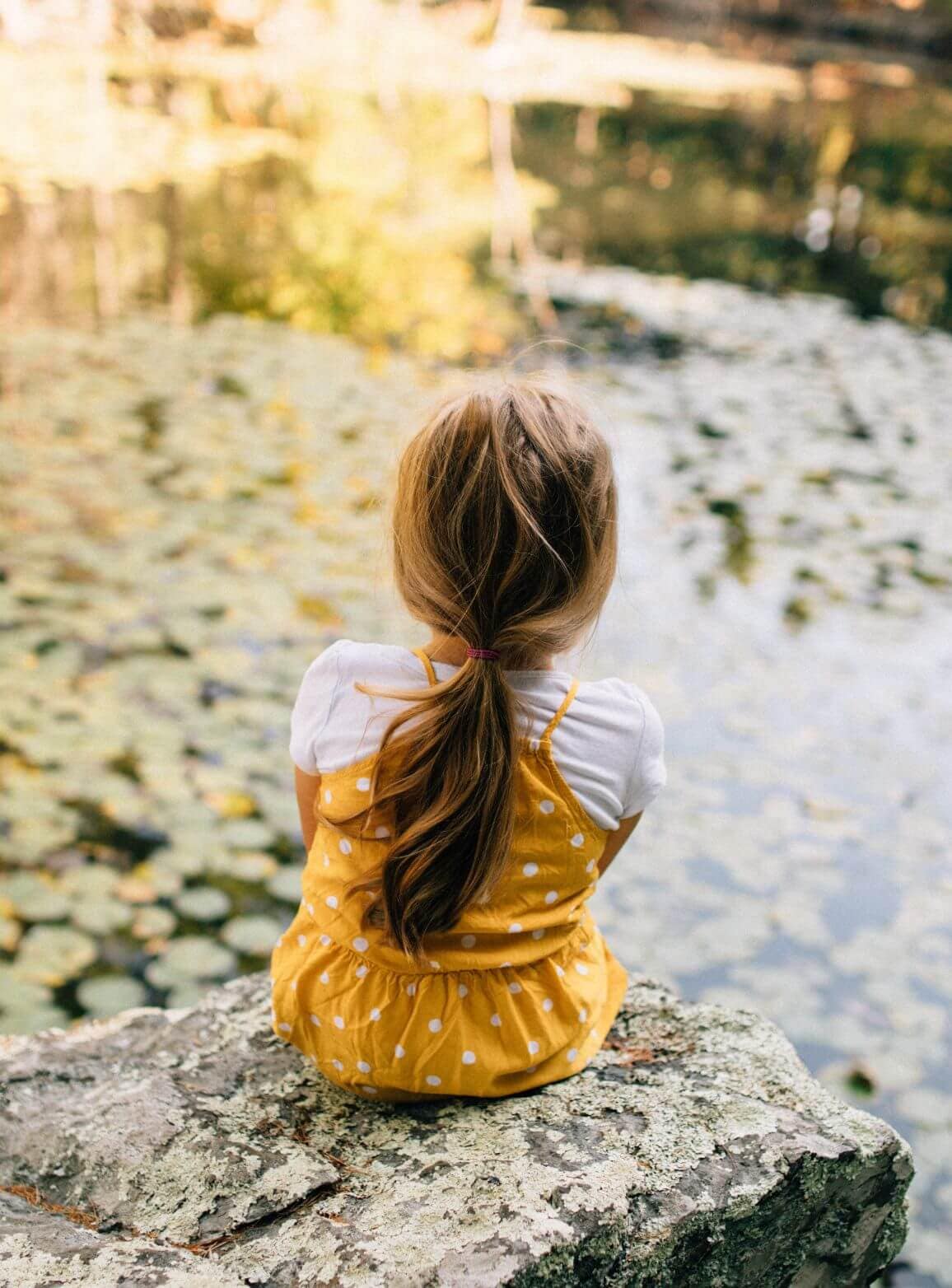 Young child sitting beside a peaceful lakeside setting near Rocklin Burke Mountain, showcasing the family-friendly outdoor lifestyle connected to nature in StreetSide’s Coquitlam community.