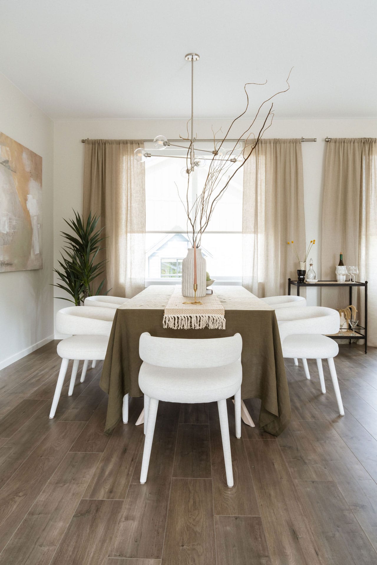 Dining room at Fox & Aikins presale development in South Surrey by Park Ridge Homes, 1871 165A Street, showcasing wide plank wood flooring, upholstered chairs, large windows with linen curtains, modern chandelier, and neutral interior design.