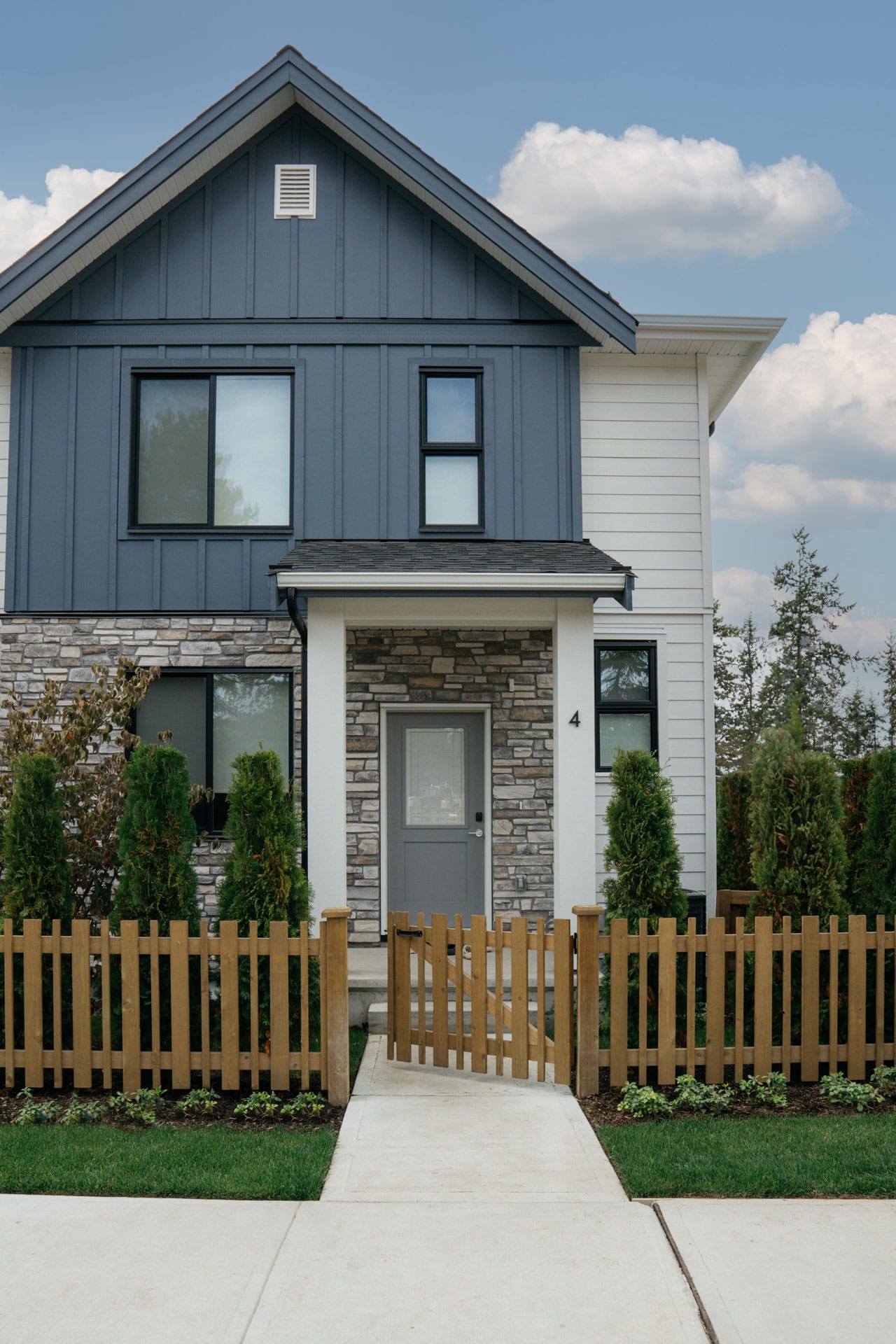 Exterior of Fox & Aikins townhome in South Surrey by Park Ridge Homes, 1871 165A Street, featuring board and batten siding, stone faรงade accents, pitched roofline, landscaped front yard, private entry, and wood picket fencing.