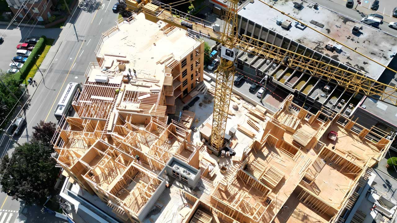 Aerial view of a presale condo building under construction in Metro Vancouver, framing exposed with a tower crane overhead