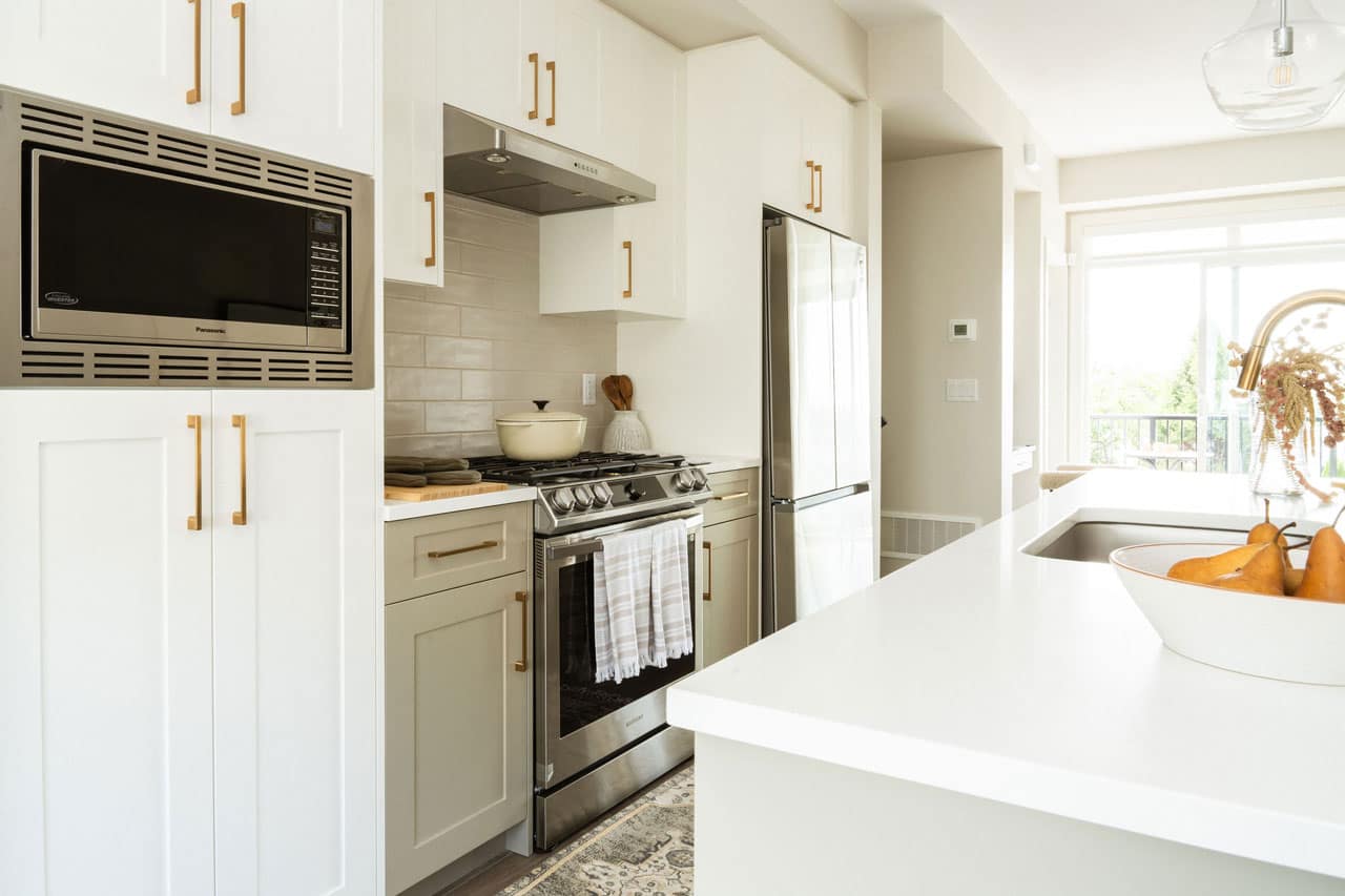 Kitchen interior at Fox & Aikins in South Surrey by Park Ridge Homes, 1871 165A Street, highlighting stainless steel gas range, built-in microwave, quartz countertops, white shaker cabinetry with gold hardware, and spacious island workspace.