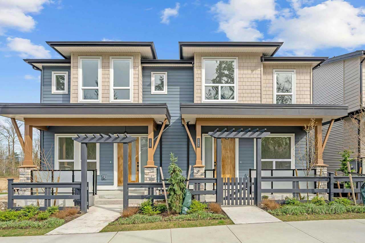 Contemporary duplex homes at Latimer Landing Langley by Archstone, located at 7760 196 Street in Langley. The exterior features modern West Coast architecture with contrasting blue and beige siding, expansive windows, covered front porches, decorative pergolas, landscaped front yards, and private fenced outdoor spaces within this master-planned community.
