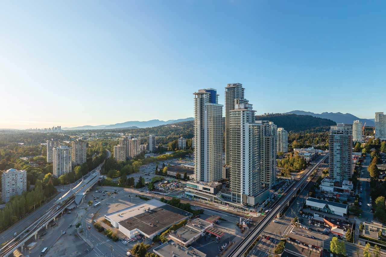 Aerial view of The City of Lougheed Burnaby, a master-planned presale community by Shape Properties at 9850 Austin Road, featuring high-rise residential towers beside Lougheed Town Centre SkyTrain Station with surrounding Burnaby neighbourhoods, mountain views, and transit connections.