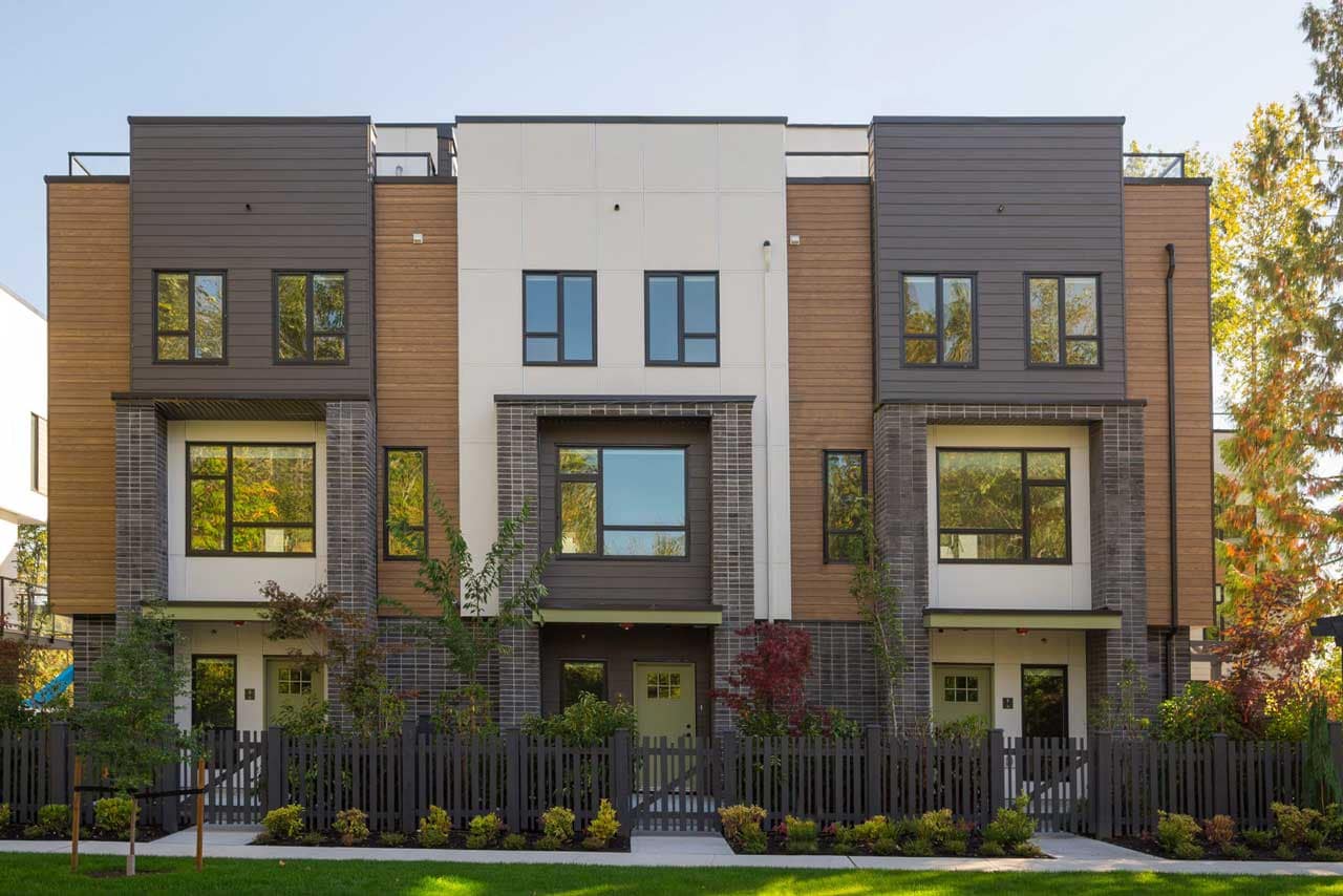 Front exterior view of modern three-storey townhomes at Park Avenue Langley, a presale development by Apcon Group located at 7946 204 Street in Langley's Yorkson neighbourhood, featuring contemporary architecture, rooftop patios, landscaped walkways, fenced front yards, and a stylish mix of wood-tone, brick, and panelled exterior finishes.