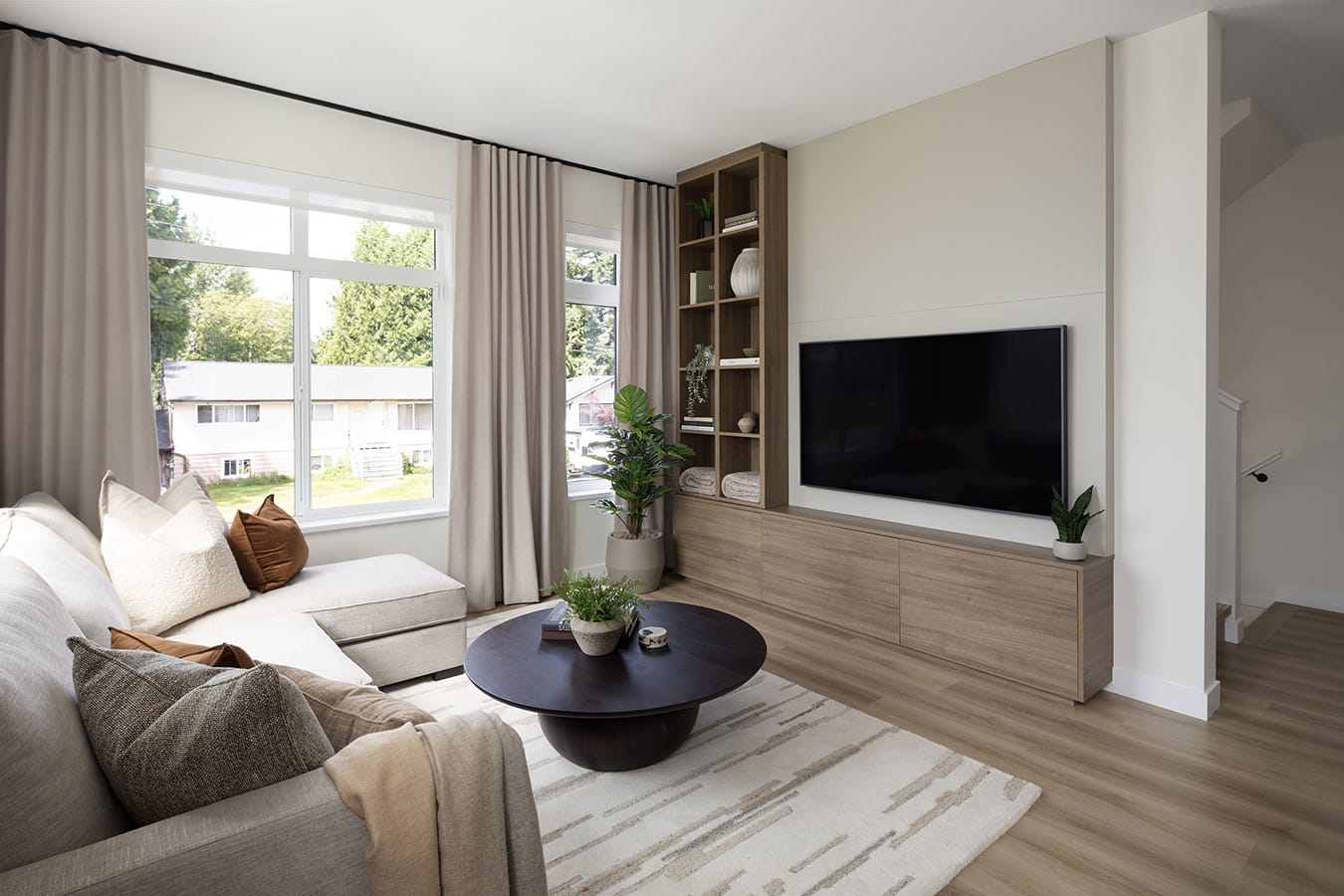 Bright living room at Rindall Port Coquitlam showcasing large windows, neutral finishes, wide-plank flooring, and custom built-in media cabinetry designed by Woodbridge Homes in Central Port Coquitlam.