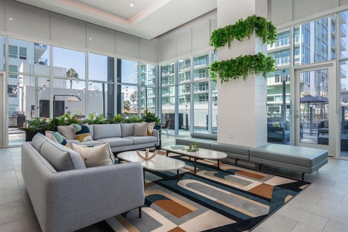Contemporary residents' lounge at Pine & Glen Coquitlam featuring comfortable seating, floor-to-ceiling windows, indoor greenery, and direct access to outdoor amenity spaces at 1175 Pinetree Way.