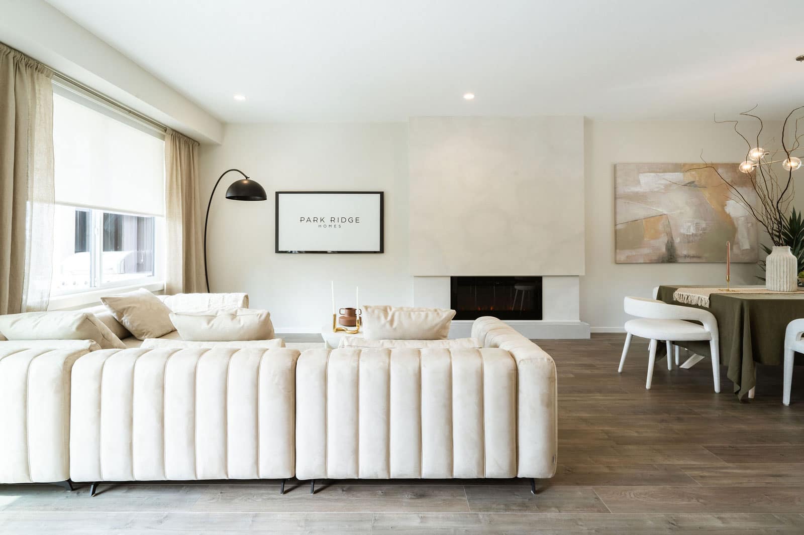 Open living and dining area at Fox & Aikins presale development in South Surrey by Park Ridge Homes, located at 1871 165A Street, featuring a sectional sofa, contemporary fireplace, wide plank flooring, large windows, and staged dining area with modern lighting.