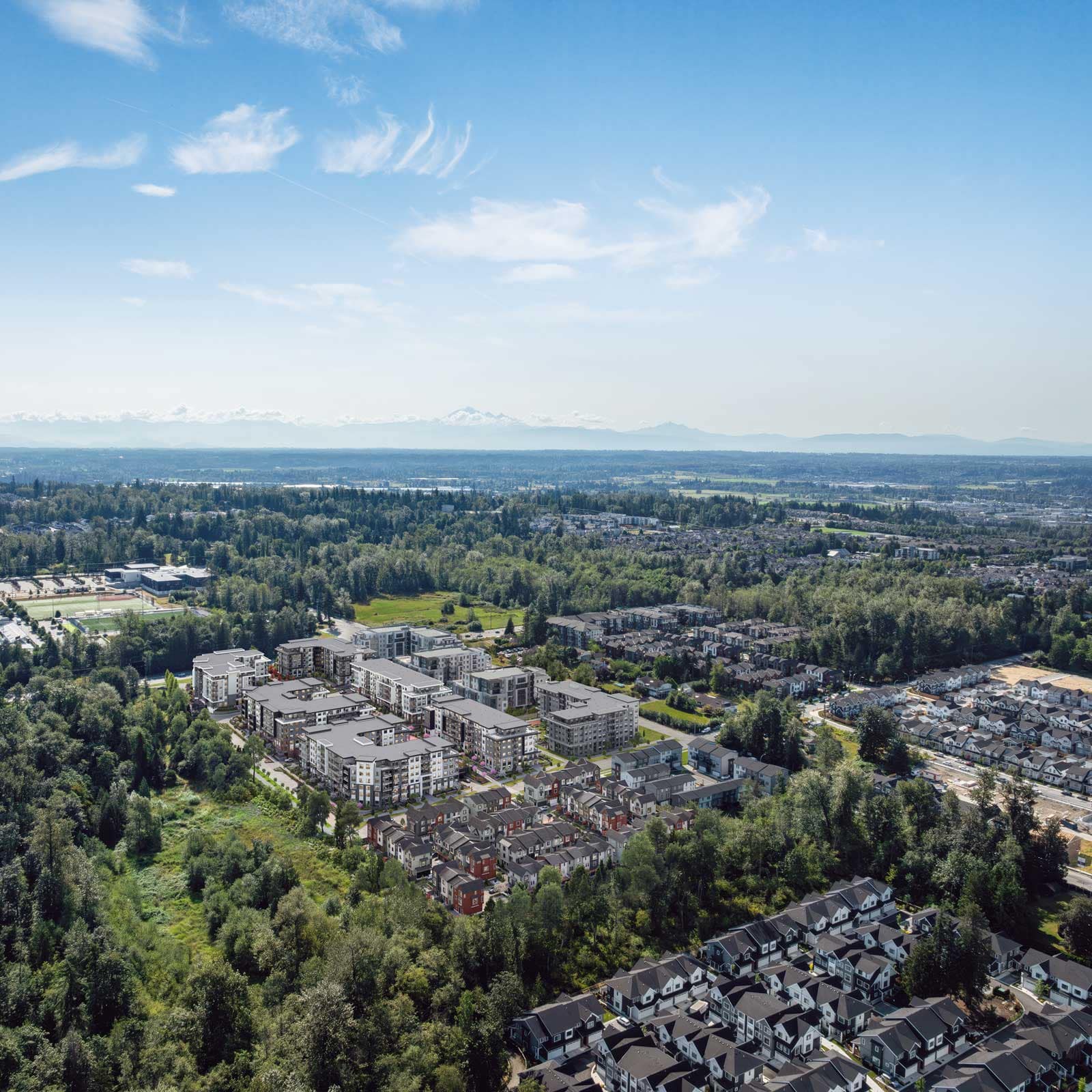 Aerial view of Langley presale condos and new construction homes, showing mid-rise buildings, townhomes, and surrounding residential communities with green space and distant mountain views.