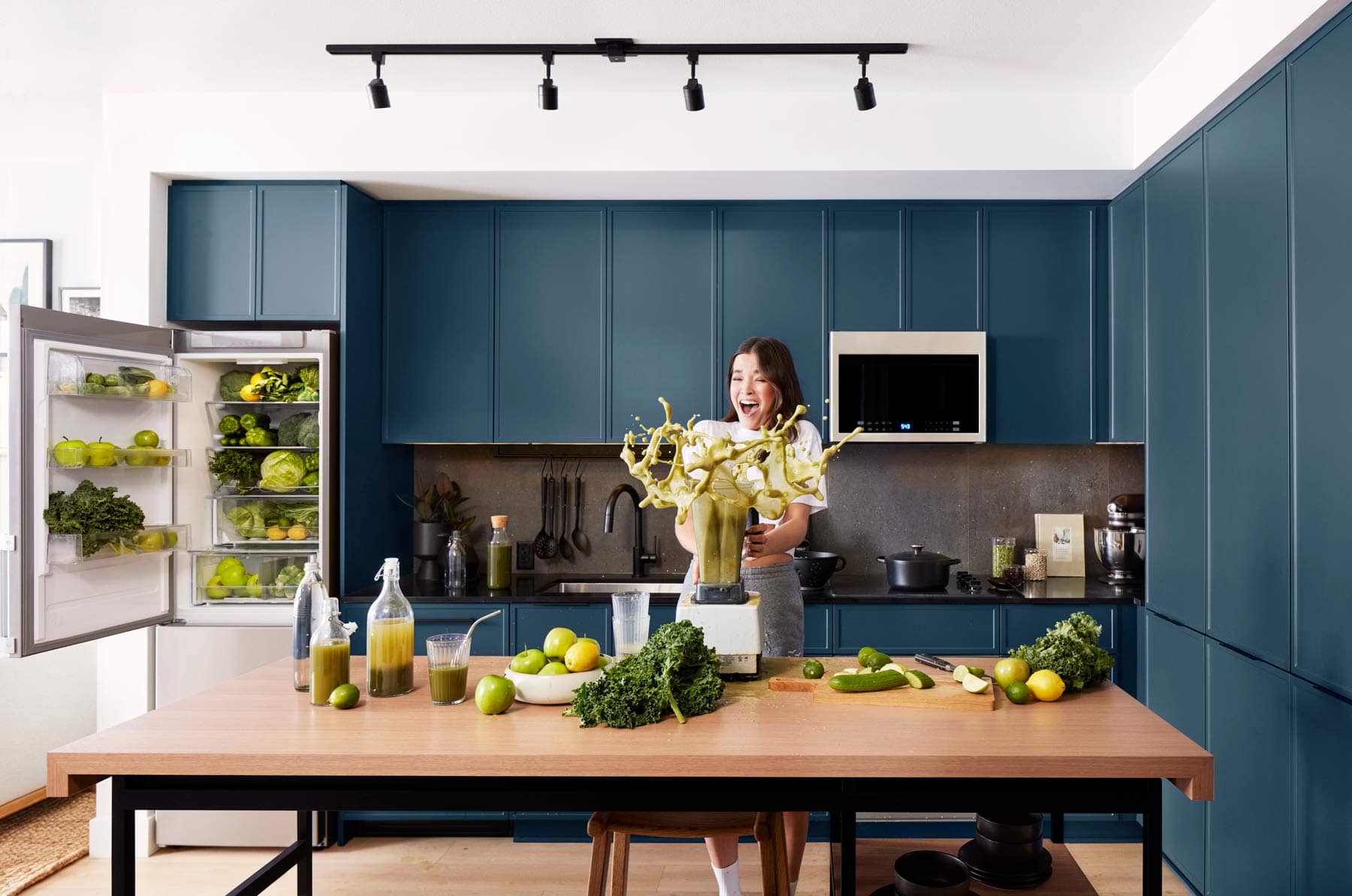 Moody Yards Port Moody kitchen with blue cabinetry and lifestyle scene featuring cooking and fresh ingredients by Mosaic at 3015 Murray Street