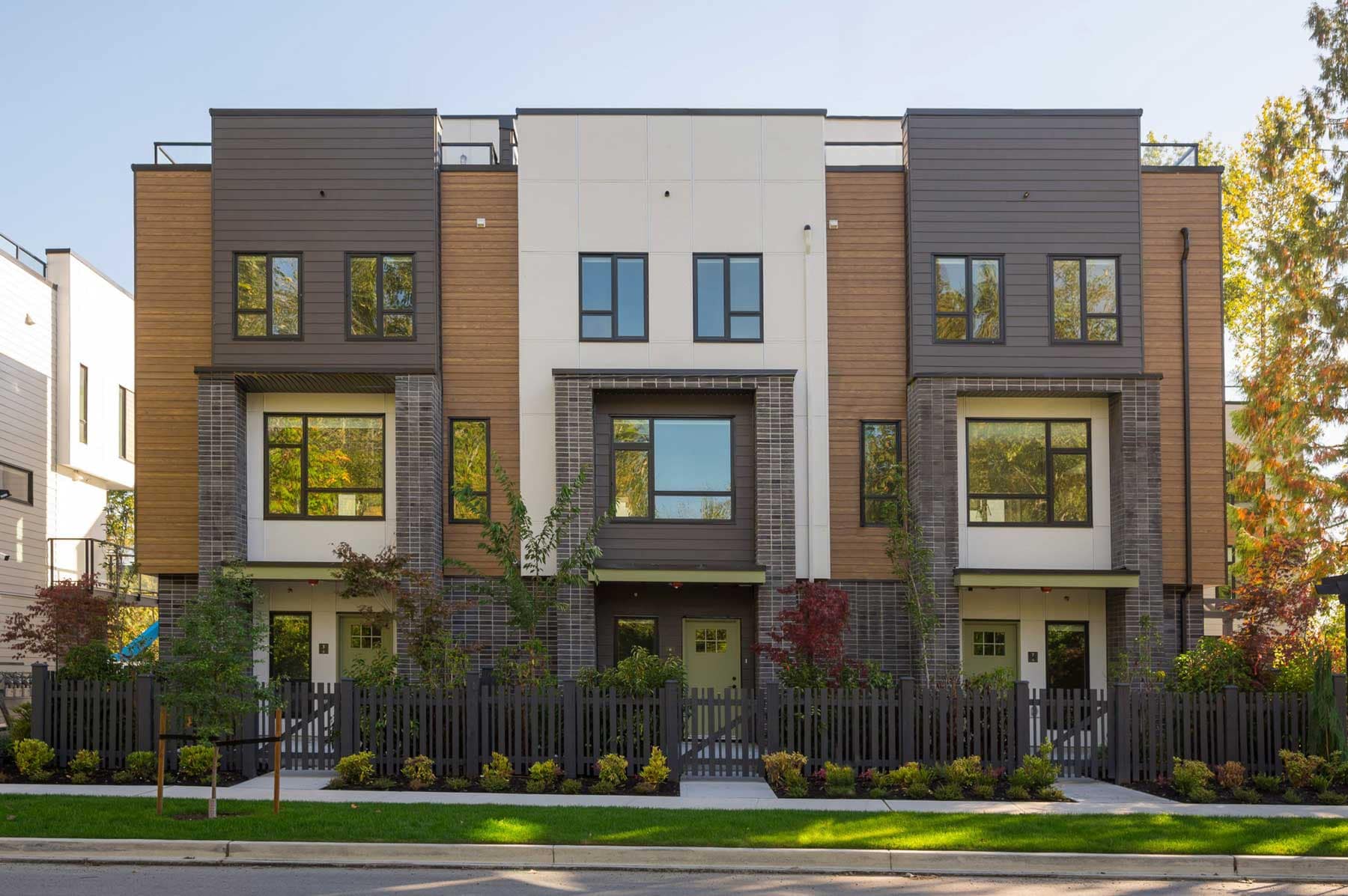 Modern exterior of Park Avenue Langley townhomes by Apcon Group at 7946 204 Street in Willoughby, Langley, featuring contemporary architecture, fenced front yards, large windows, and rooftop patio access.