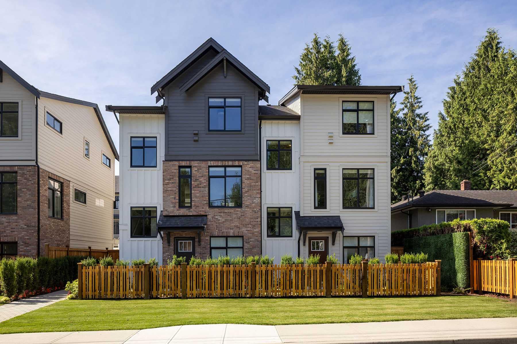 Exterior view of Rindall Port Coquitlam townhomes showcasing a blend of red brick, modern siding, pitched rooflines, and private fenced yards in a Woodbridge Homes community at 2150 Rindall Avenue in Central Port Coquitlam.