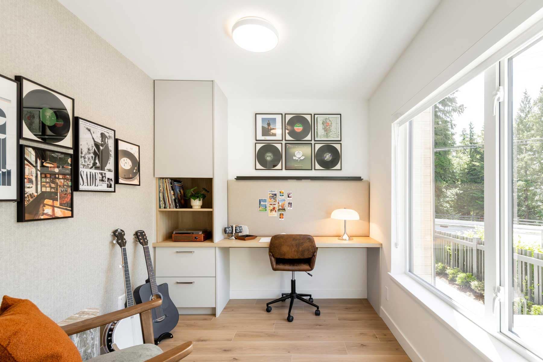 Home office nook in a Towns at Burke Coquitlam townhome with a built-in desk, framed vinyl records on the wall, guitars, and a large window overlooking the street.