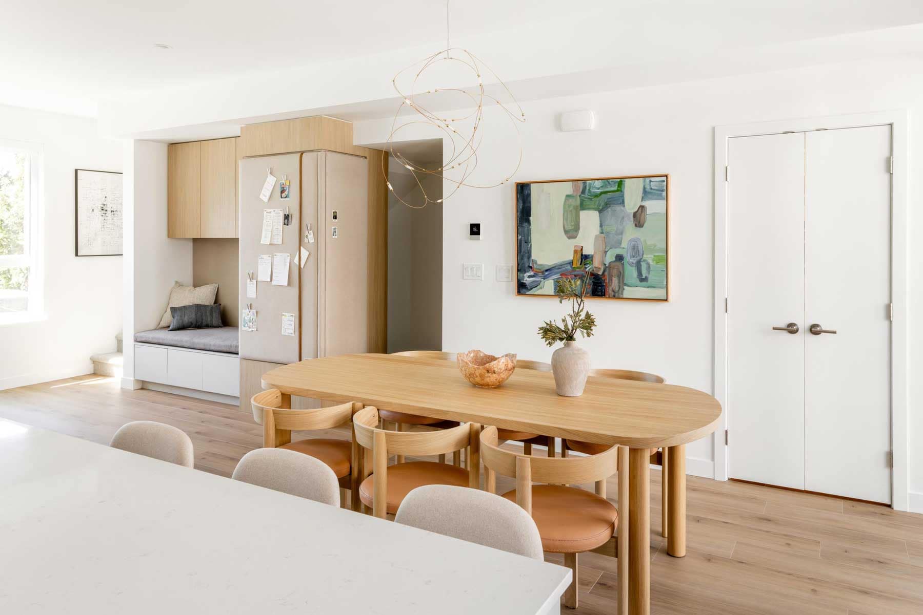 Dining area in a Towns at Burke Coquitlam townhome with an oval wood table, leather-seated chairs, a built-in banquette, and abstract artwork on the wall.