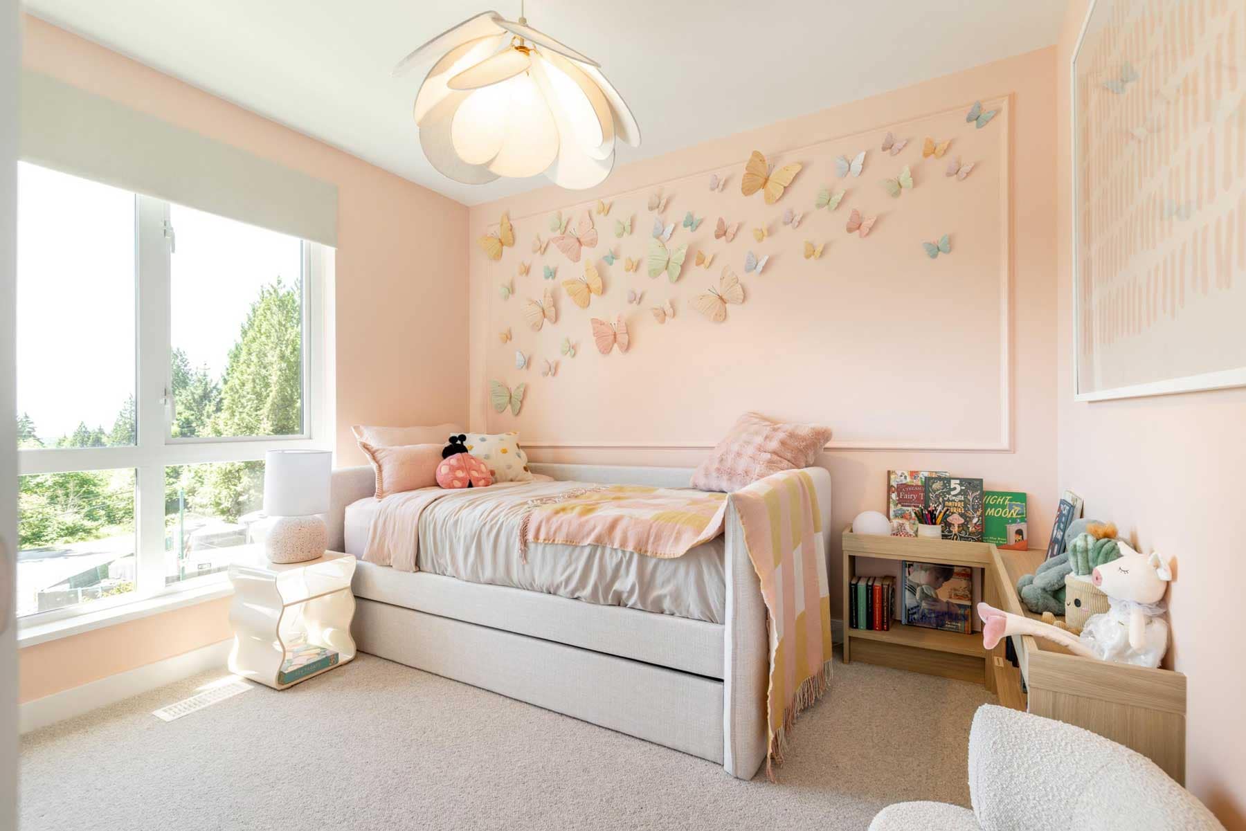 Kids bedroom in a Towns at Burke Coquitlam townhome painted soft pink with a paper butterfly wall display, upholstered daybed, and a bookshelf with children's books.