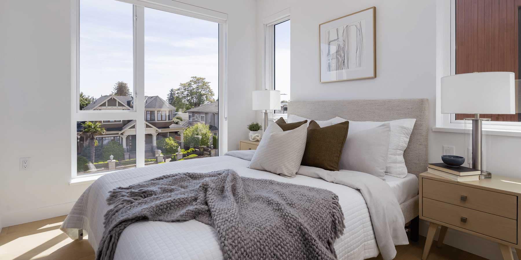 Primary bedroom interior at Be W 49th Vancouver in Oakridge featuring oversized corner windows, soft neutral finishes, wood flooring, and natural light inside the boutique townhouse development by Modella Developments at 715 West 49th Avenue.