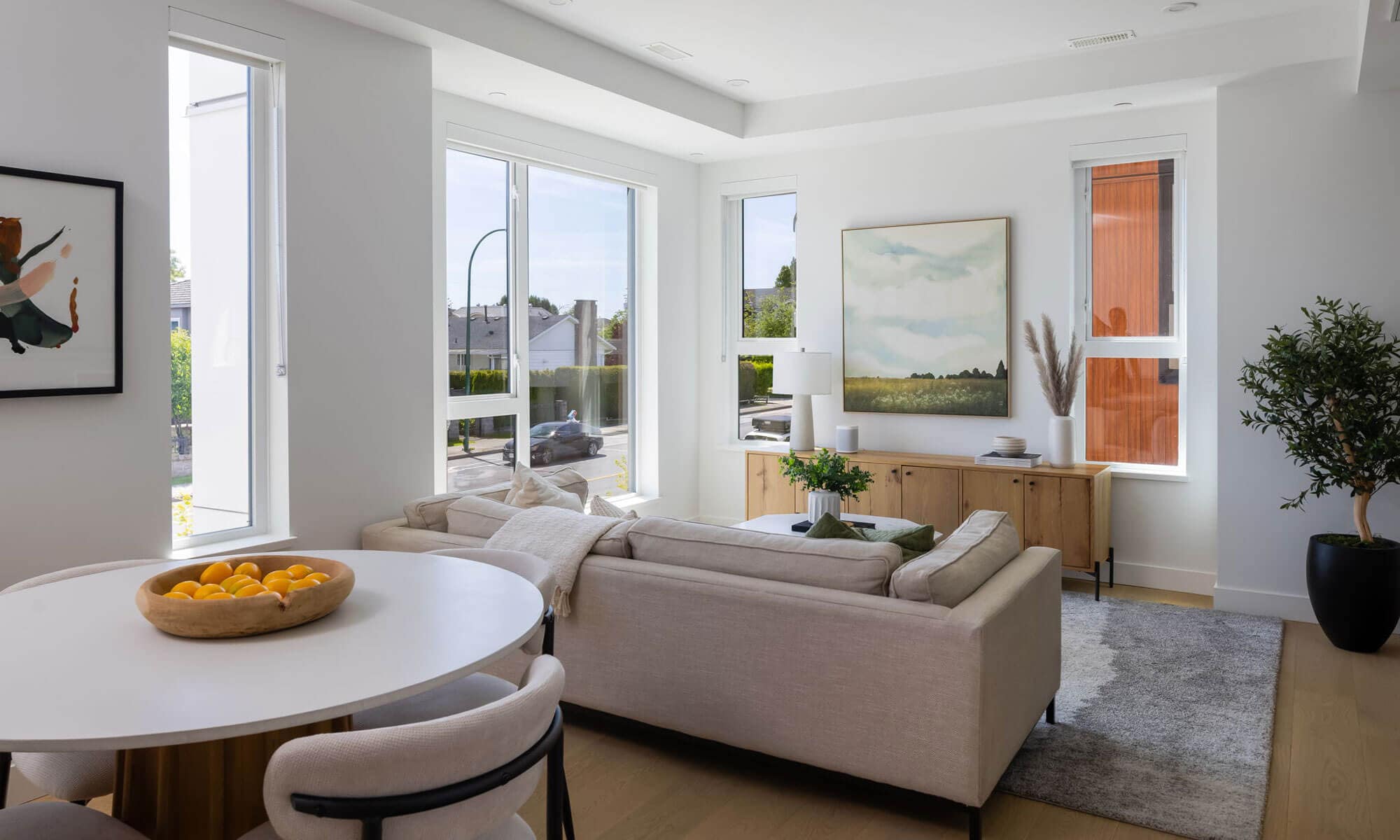 Open-concept living and dining area at Be W 49th Vancouver in Oakridge by Modella Developments, showcasing expansive windows, natural light, soft neutral interiors, engineered wood flooring, and modern West Side townhouse design at 715 West 49th Avenue.