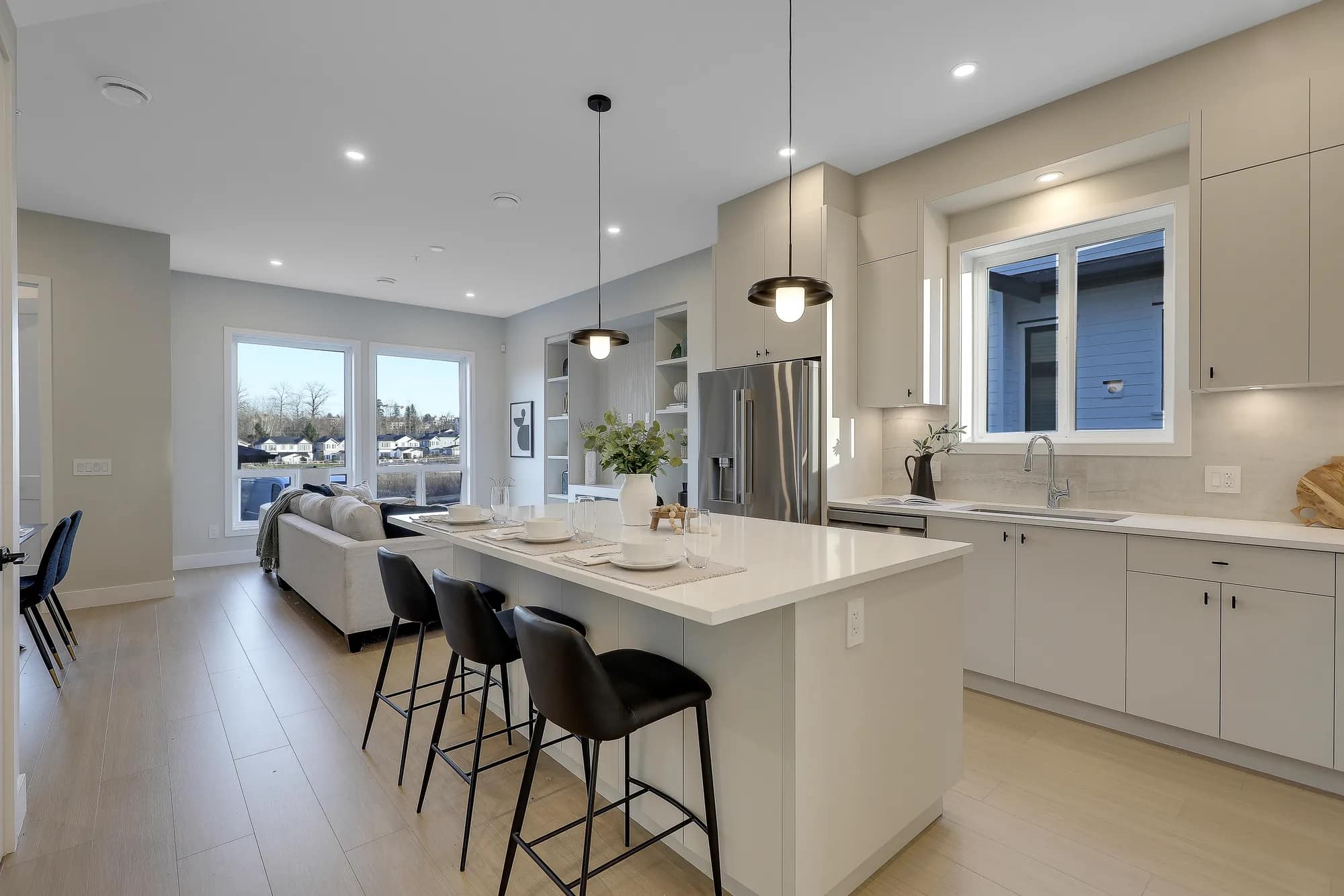 Gourmet kitchen at Latimer Landing Langley by Archstone at 7760 196 Street. The kitchen features a large island with seating, quartz countertops, stainless steel appliances, custom cabinetry, pendant lighting, and an open-concept layout overlooking the living room.
