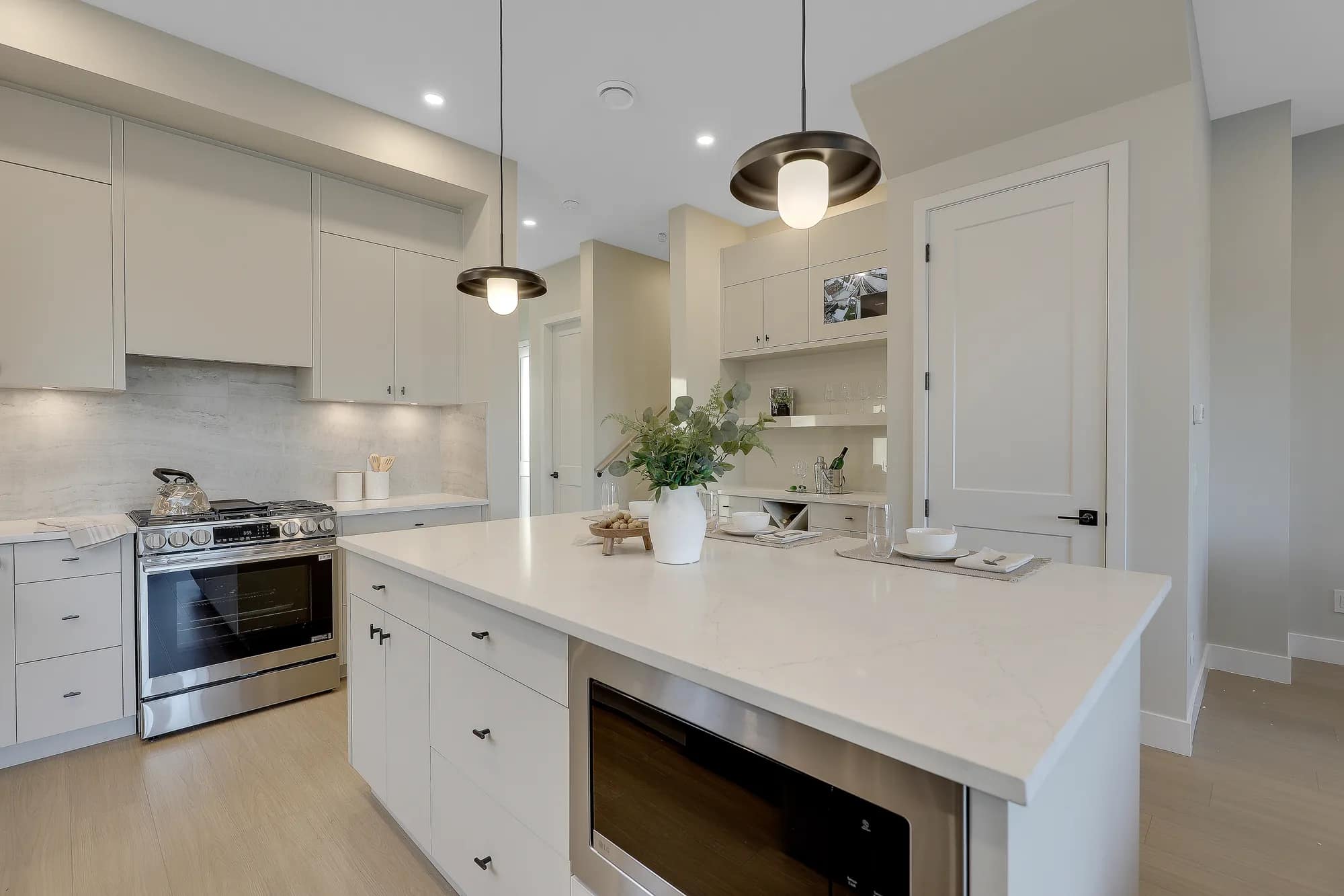 Contemporary kitchen at Latimer Landing Langley by Archstone featuring a large quartz island, integrated microwave drawer, stainless steel appliances, full-height cabinetry, pendant lighting, and open-concept design at 7760 196 Street in Langley.