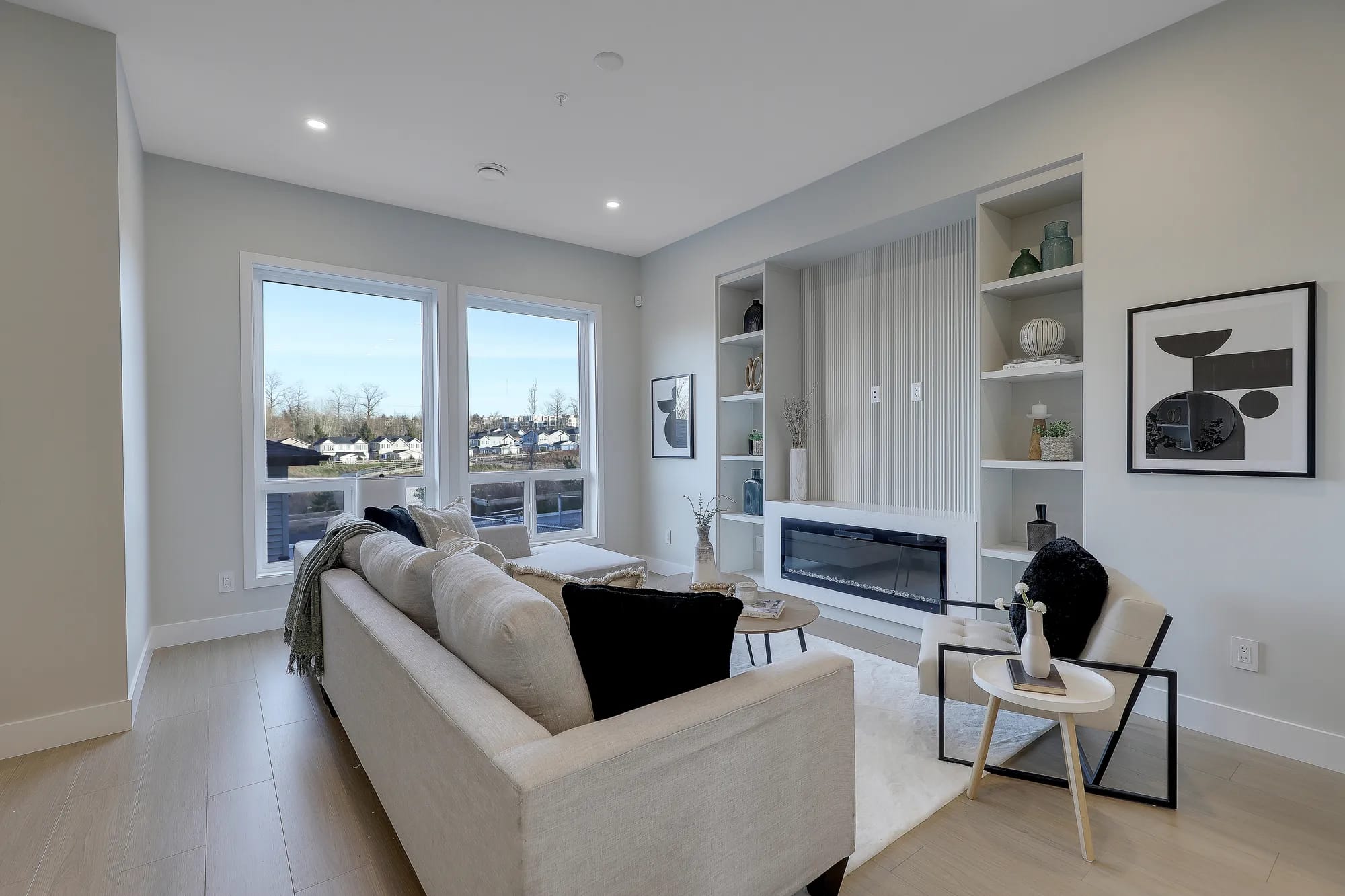 Contemporary living room at Latimer Landing Langley by Archstone, located at 7760 196 Street. The space includes a modern fireplace feature wall, built-in shelving, large windows, neutral finishes, and designer furnishings.