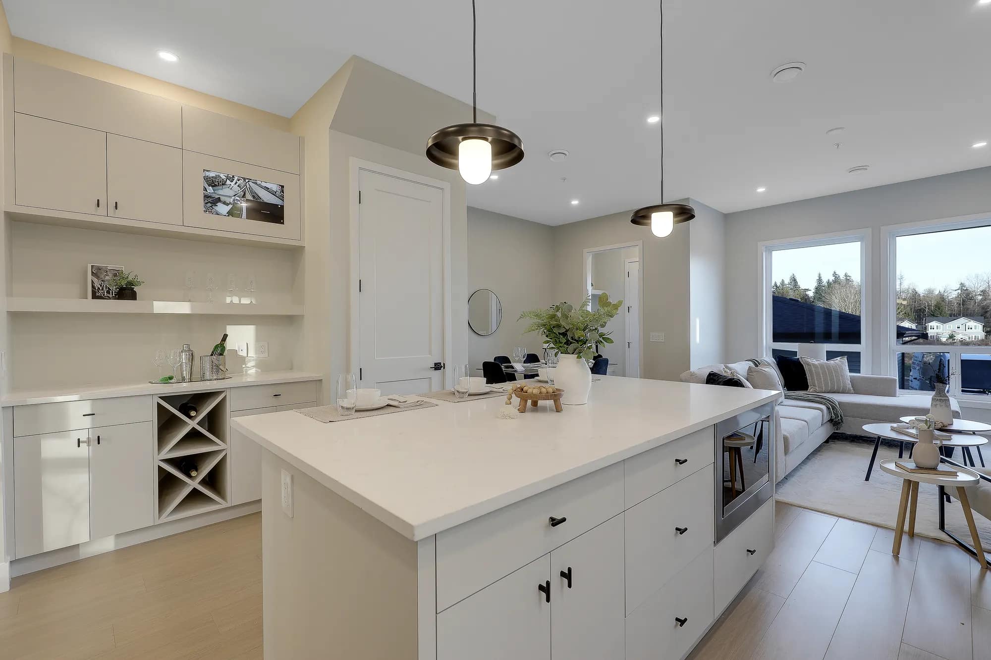 Open-concept kitchen and living space at Latimer Landing Langley by Archstone. Features include a large quartz island, custom built-in cabinetry, pendant lighting, dining area, expansive windows, and seamless flow into the living room.